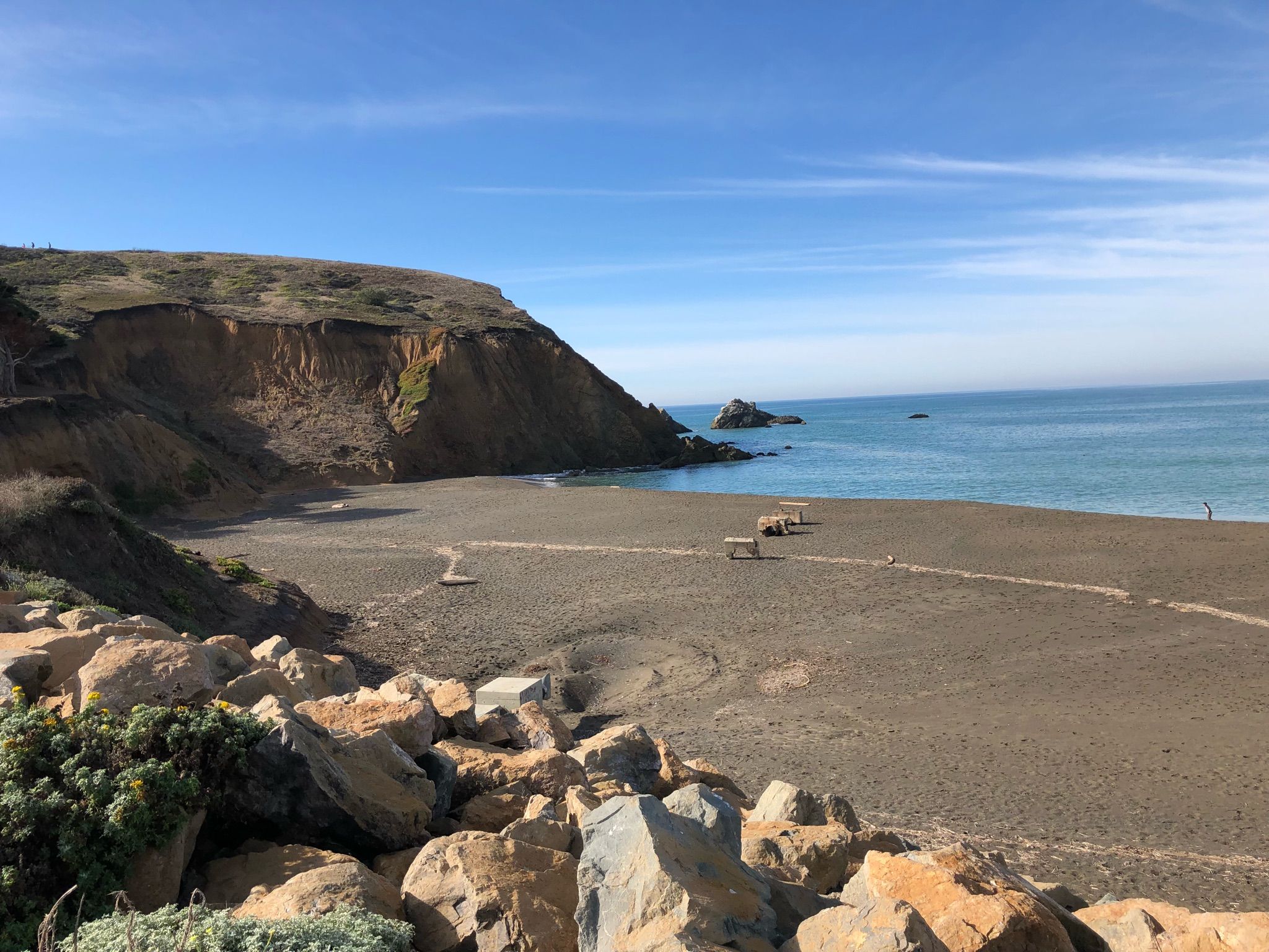 Sunny beach with dark sand, steep cliffs, and blue ocean. - Mori Point Loop Trail