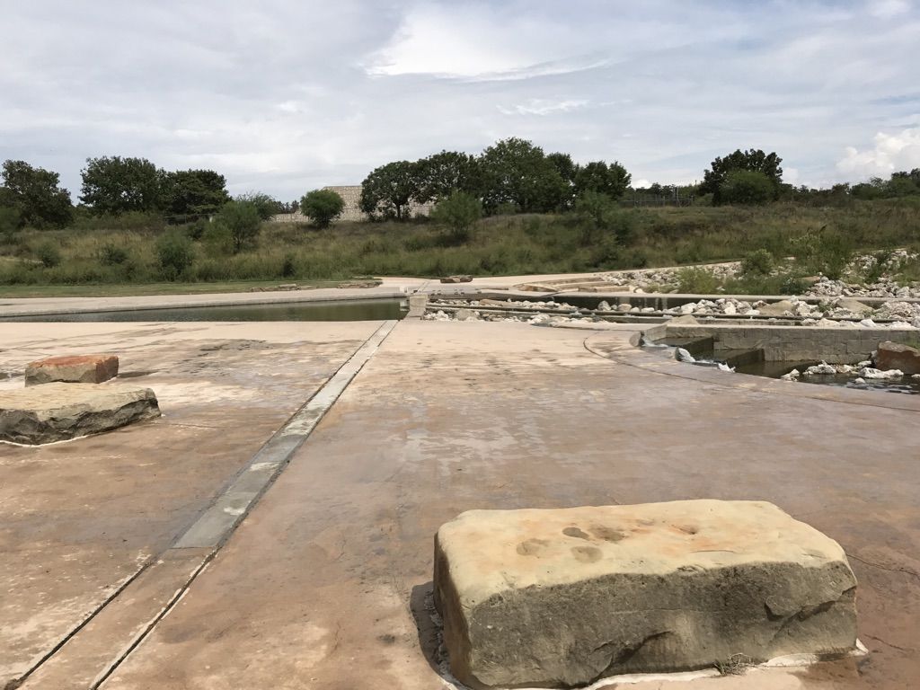 Concrete path with water features and large rocks under a cloudy sky. - River Walk Mission Reach Trail
