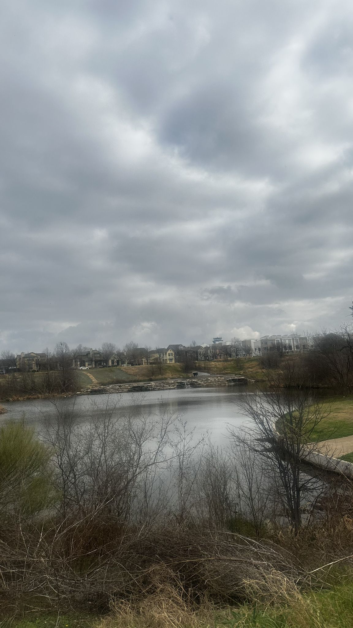 A wide lake with distant buildings and bare trees under a cloudy sky. - Mueller Trail