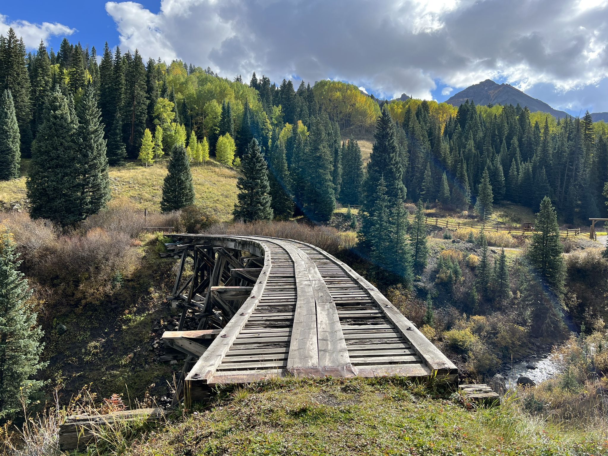 Curved wooden railroad tracks on a trestle bridge through a vibrant forest. - Galloping Goose