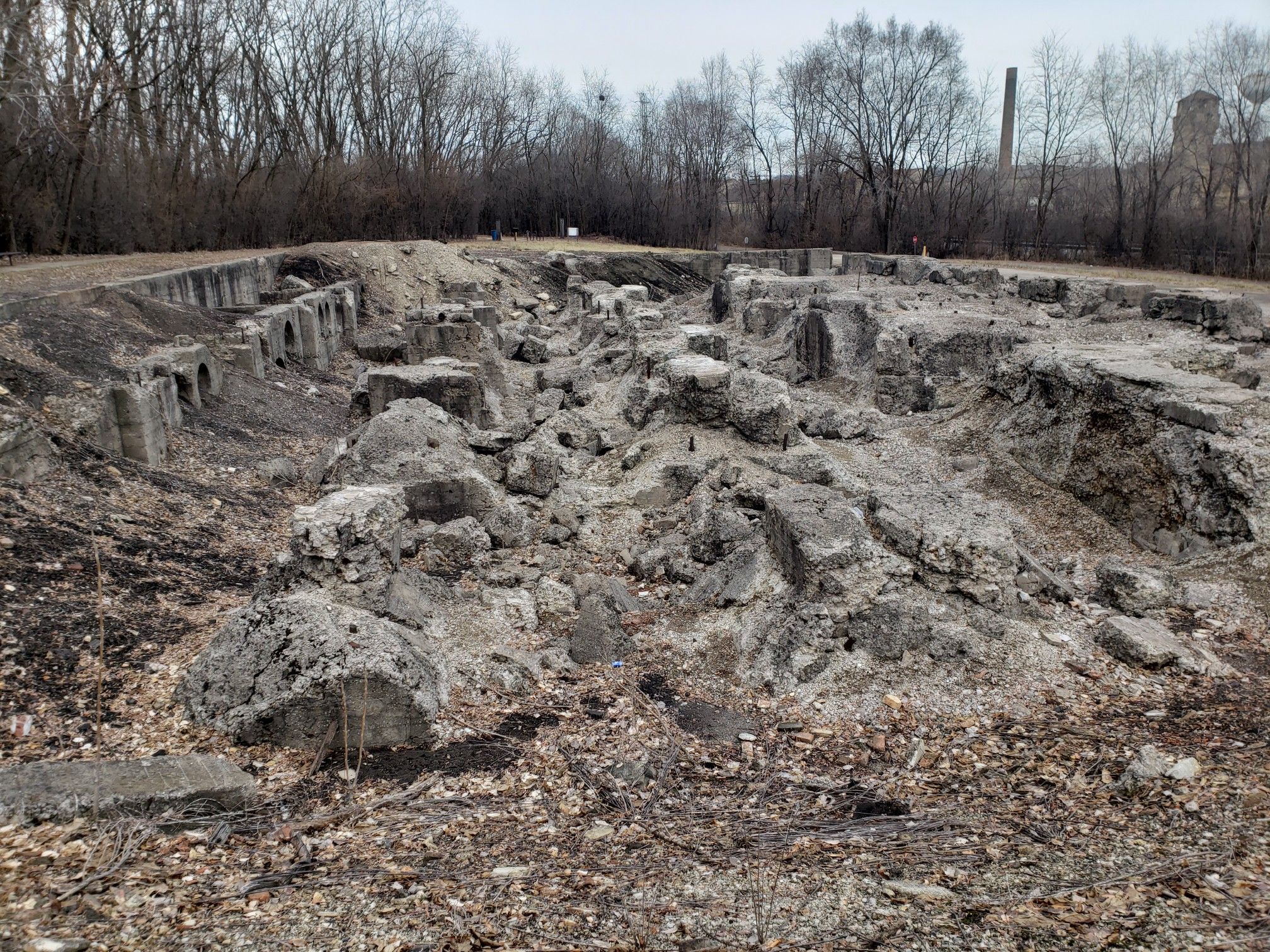 Overcast view of extensive concrete ruins and rubble with bare trees. - Joliet Iron Works Historic Site Trail