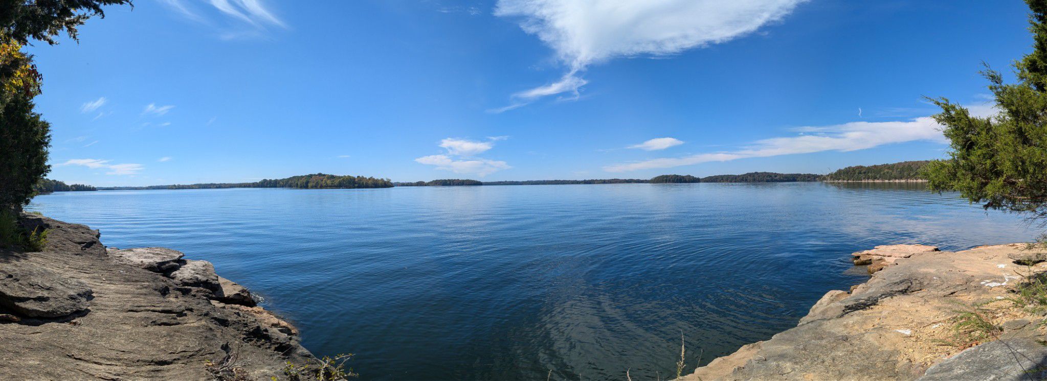 Panoramic view of a calm lake with distant islands under a bright blue sky. - Day Loop Trail
