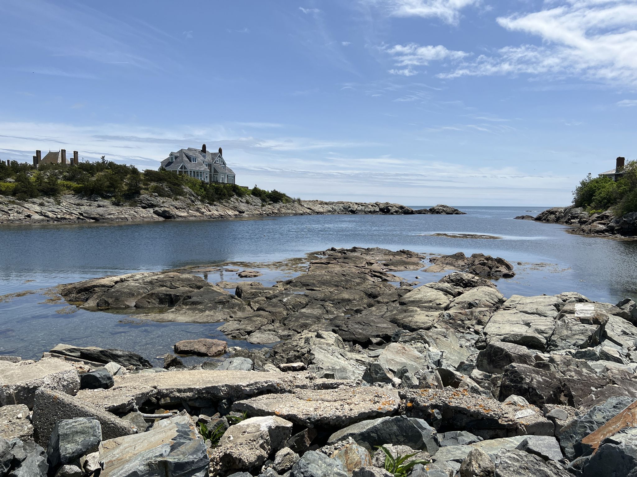 Rocky coastline with a large house on a distant hill under a bright sky. - Sachuest to Brenton Point via Ocean Drive Scenic Road