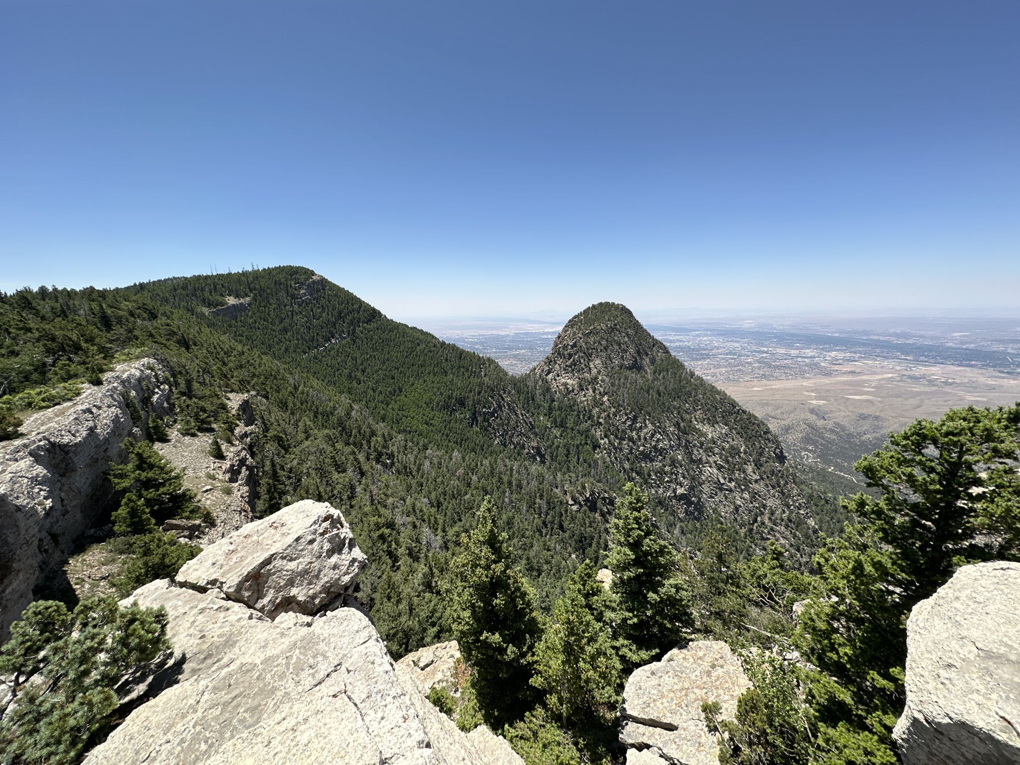 Rocky mountain viewpoint overlooking two forested peaks and a distant valley. - North Crest Trail