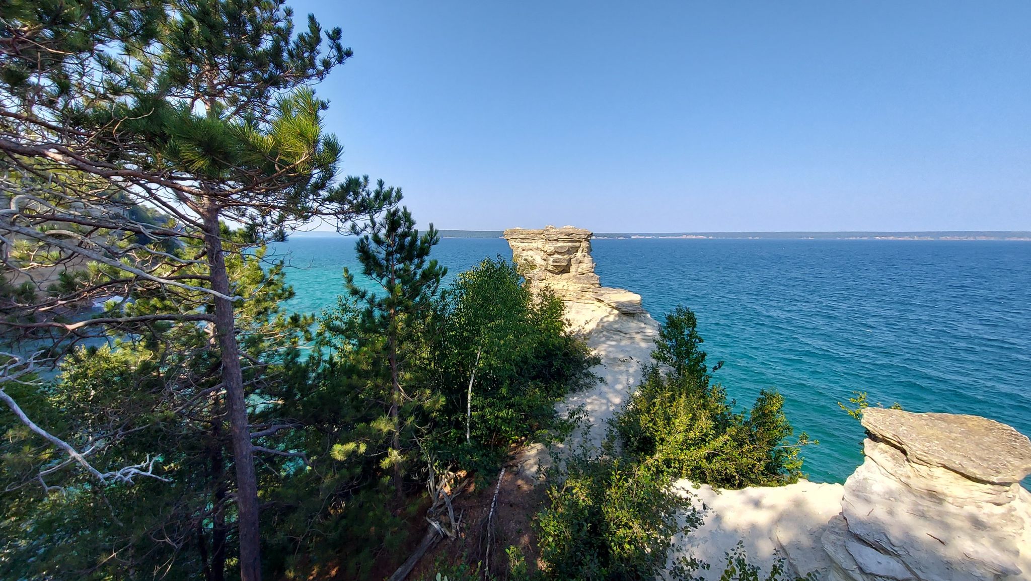 Panoramic view of rocky cliffs, green trees, and blue water on a bright day. - Miners Castle and Miners Beach
