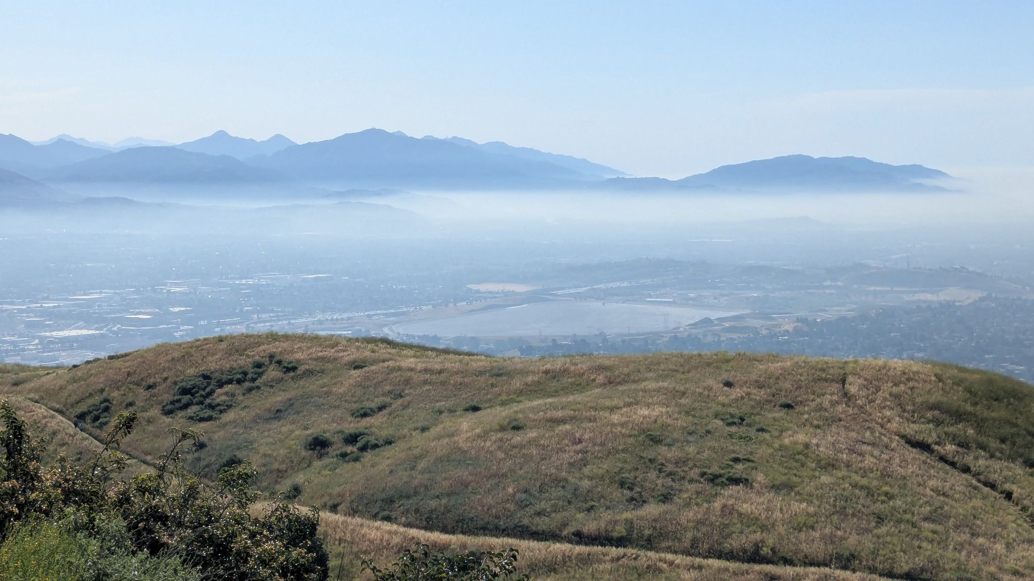 Rolling hills covered in dry grass overlooking a hazy valley and distant mountains. - Mission Point via De Campos Trail