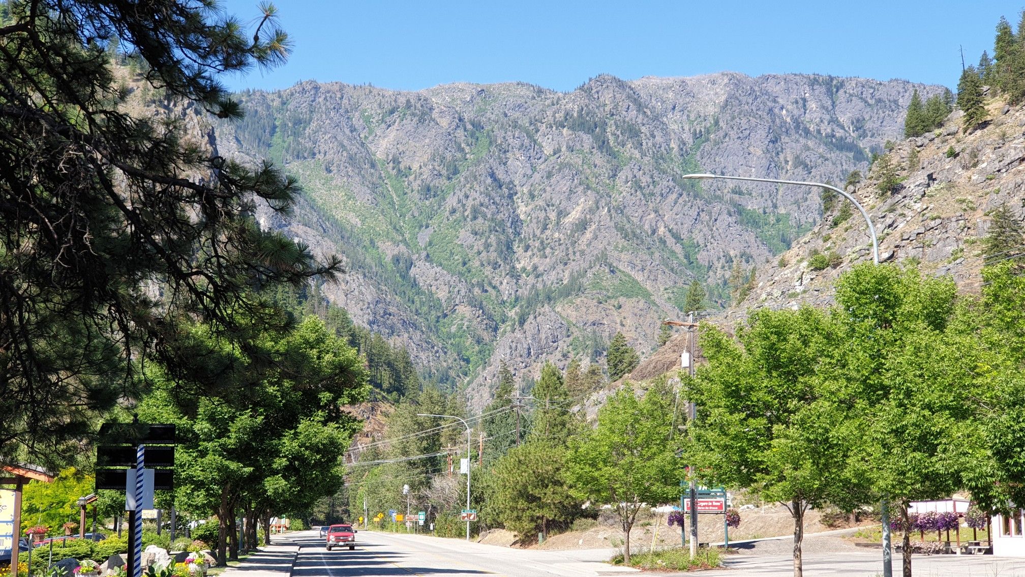 A road through a sunny, tree-lined valley with rugged mountains in the background. - Wenatchee River loop