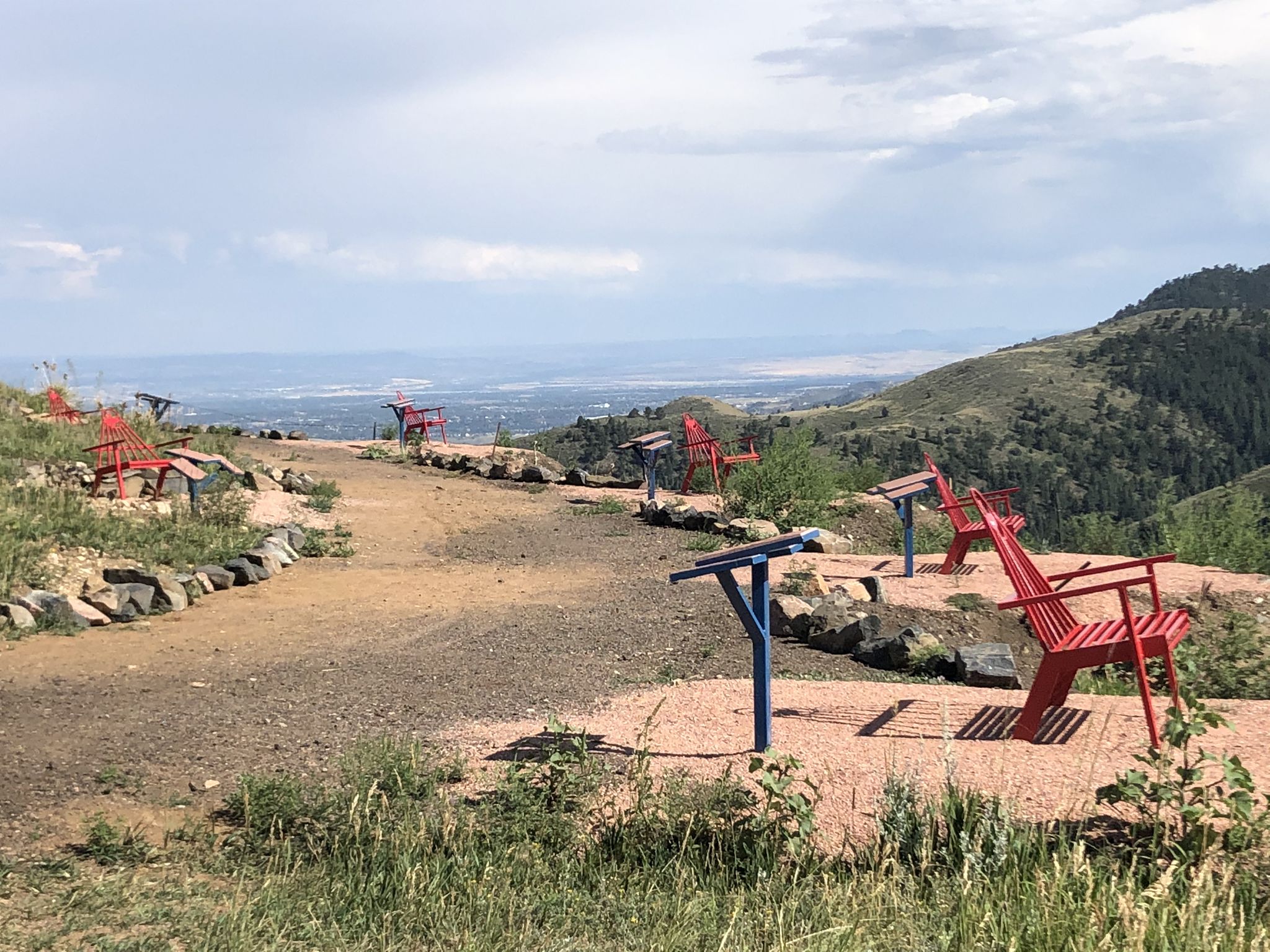 Red and blue Adirondack chairs line a dirt path on a hillside. - Mother Cabrini Shrine Climb