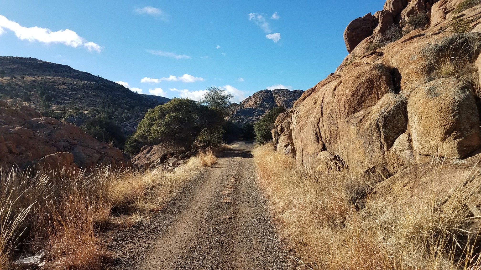 Dirt road through a rocky canyon under a bright blue sky. - Iron King Trail