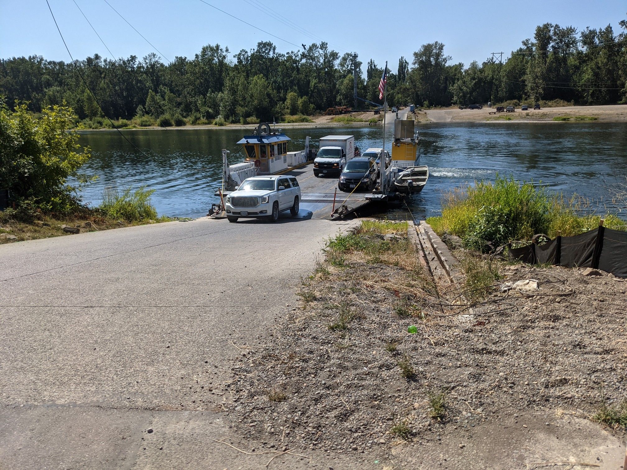 A ferry boat with cars docked at a paved ramp on a sunny day. - Willamette Mission State Park loop
