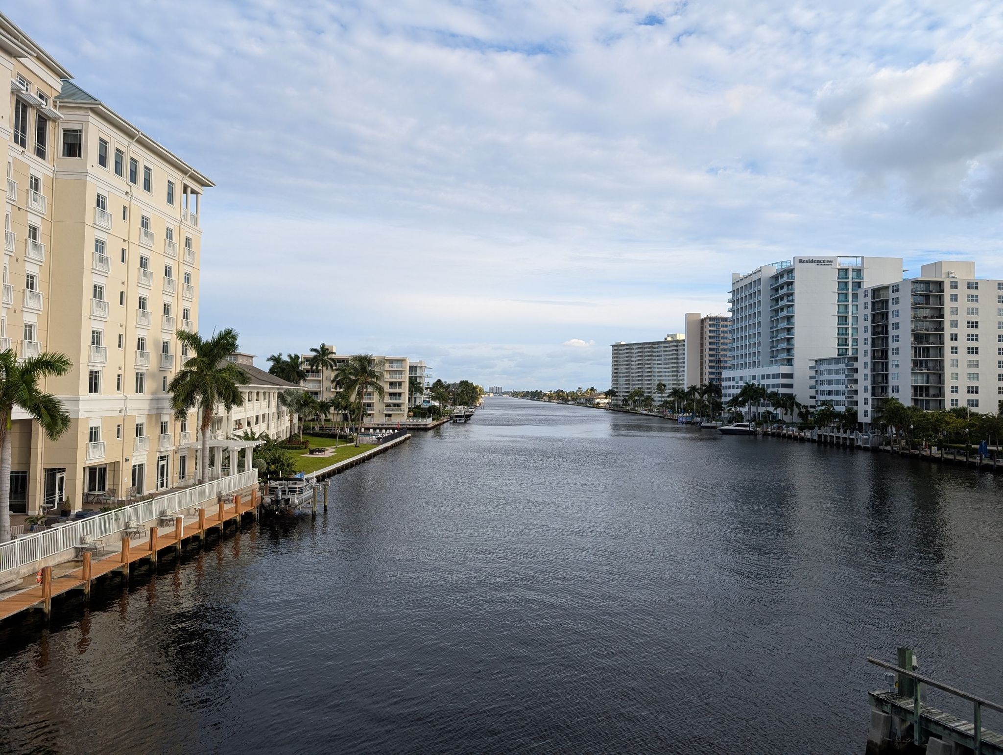 A wide canal flows between tall buildings and palm trees under a cloudy sky. - Stranahan House Museum – Hugh Taylor Birch State Park loop from Fort Lauderdale