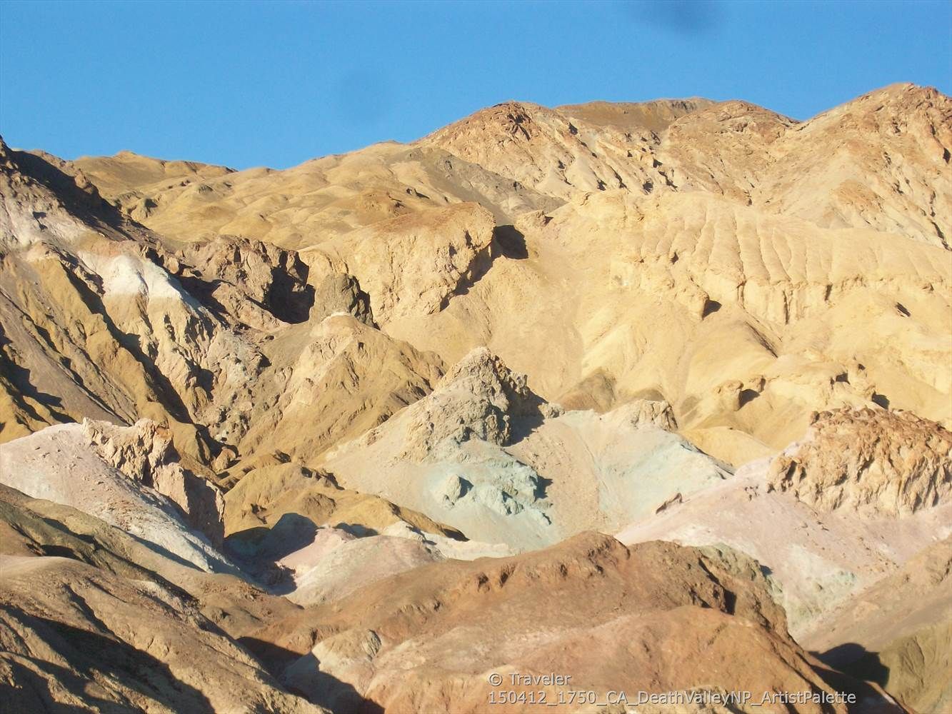 Rugged, multi-hued desert mountains bathed in bright sunlight under a clear sky. - Artist Drive Viewpoint – Artist's Palette loop from Mars Hill