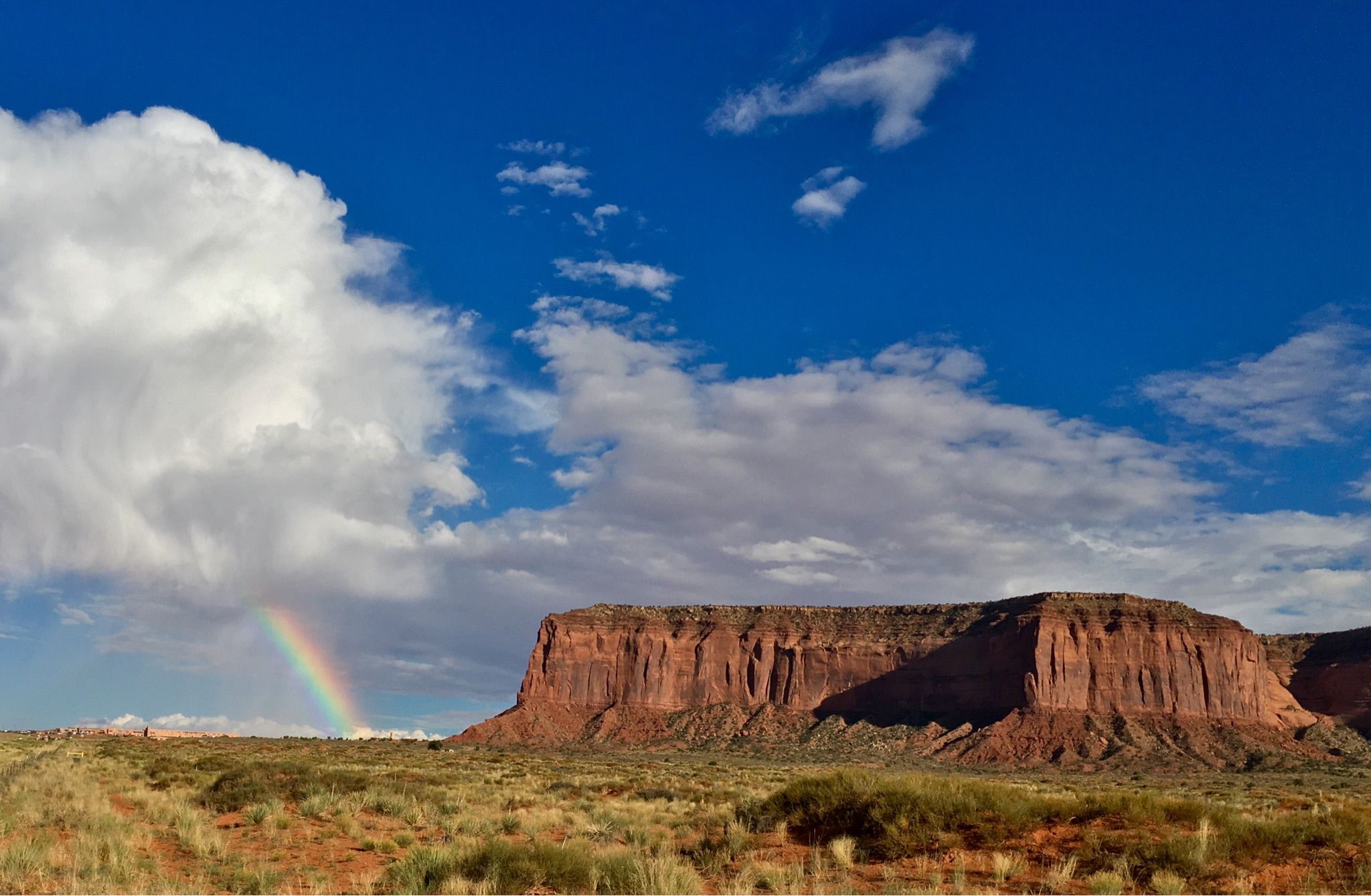 Red mesa under a bright blue sky with white clouds and a rainbow. - Monument Valley Scenic Road: Kayenta to Monument Valley