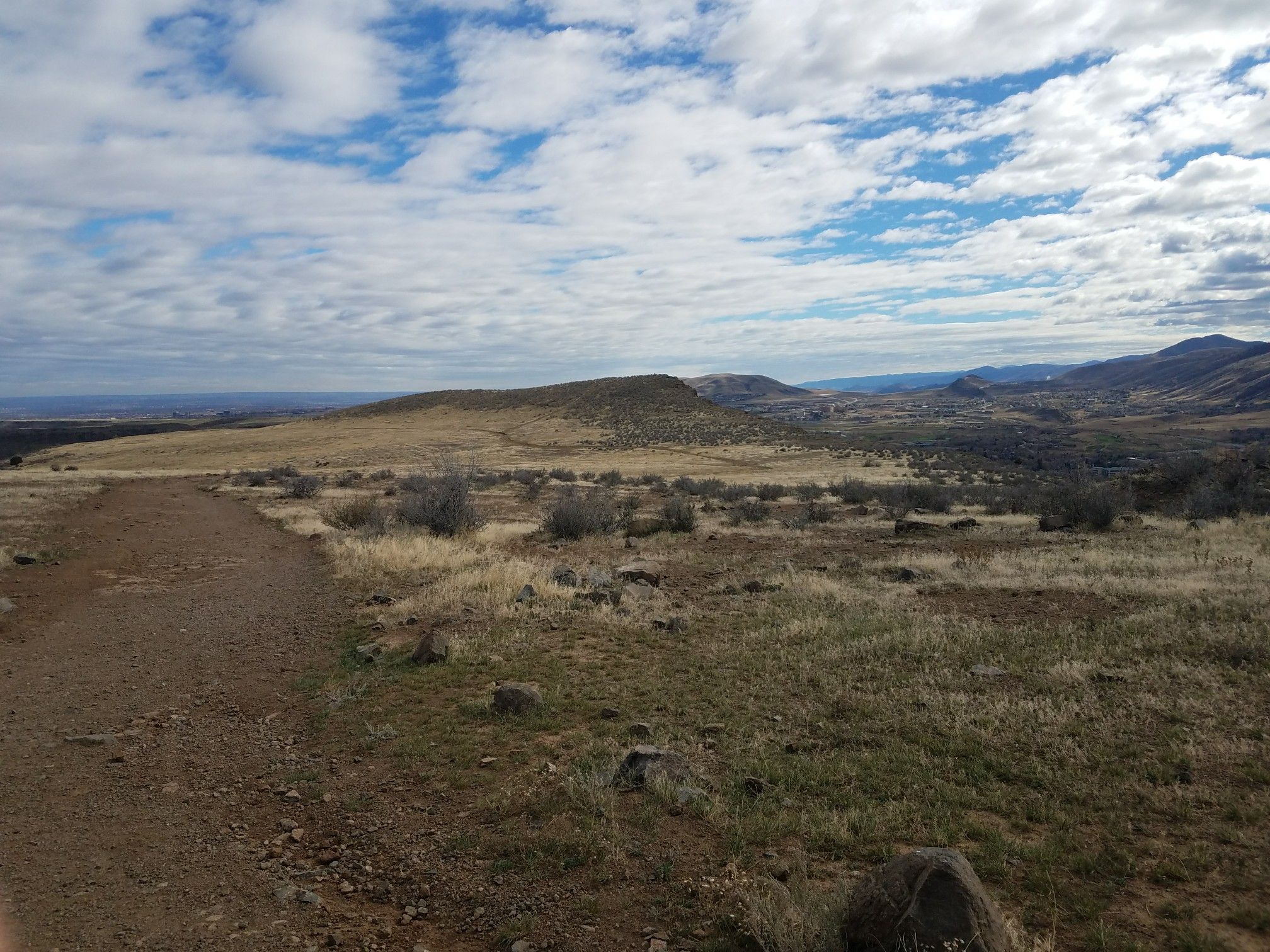 Dirt path through dry, rolling hills and plains under a partly cloudy sky. - Golden Cliffs Trail