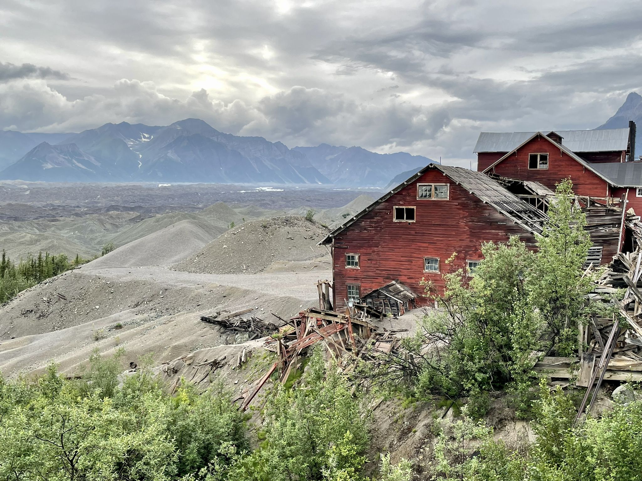 Old red buildings on a hill overlooking a vast, rocky landscape. - Root Glacier Trail