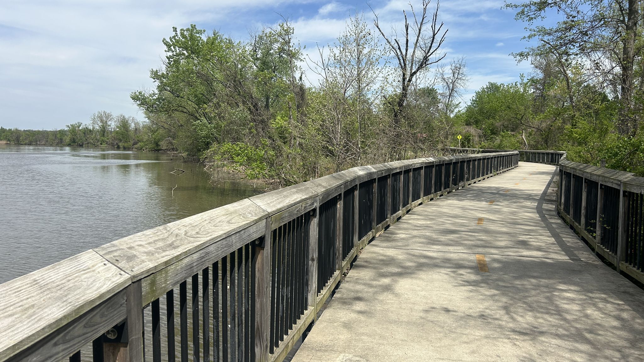 A curved wooden boardwalk alongside a calm river, surrounded by green trees. - Melrose Park Pump Track – Bladensburg Battlefield loop from Brentwood