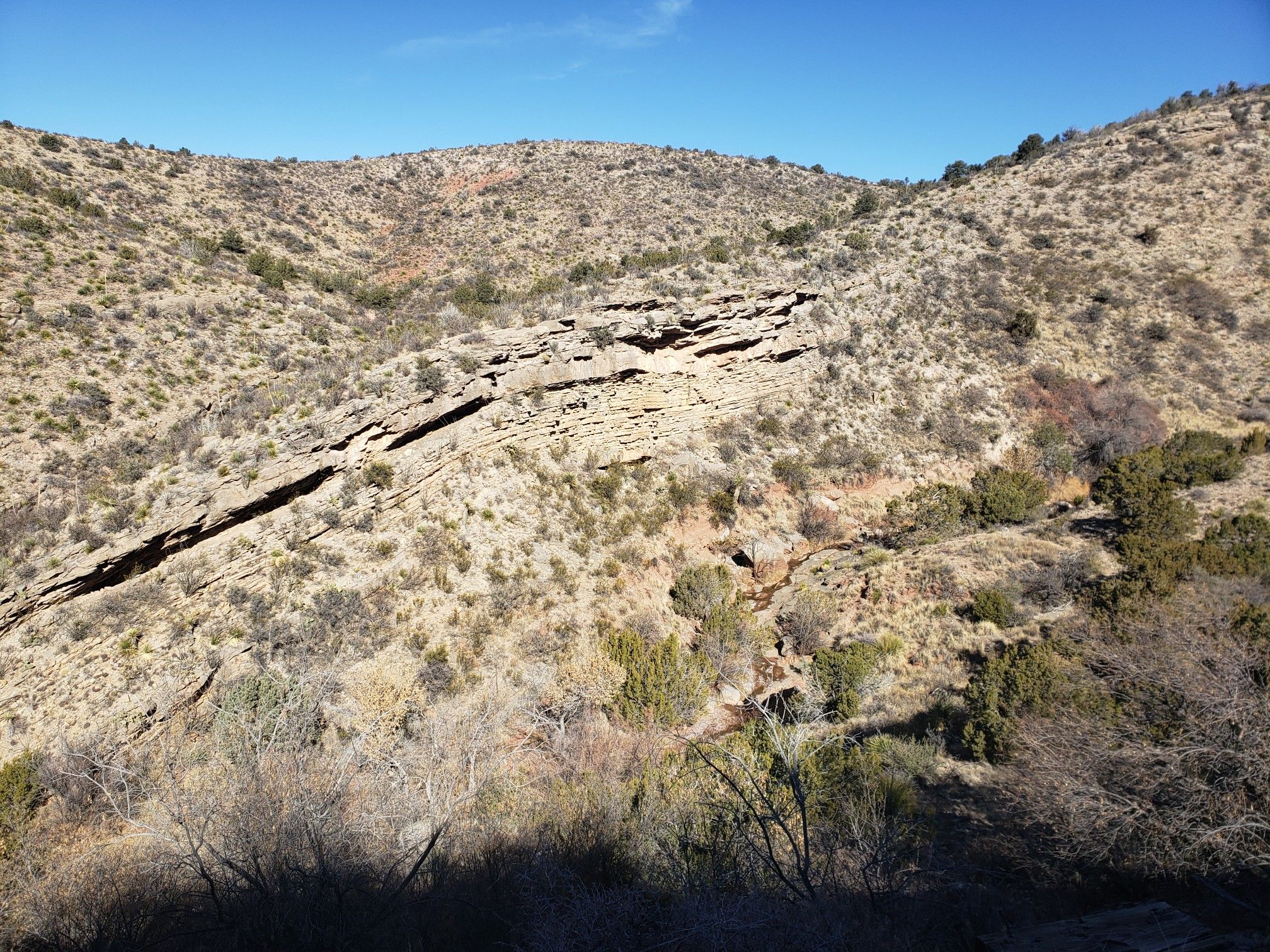 Arid, rocky hillside with sparse brush and layered rock formations under bright sun. - Bridal Veil Falls Trail (T129)