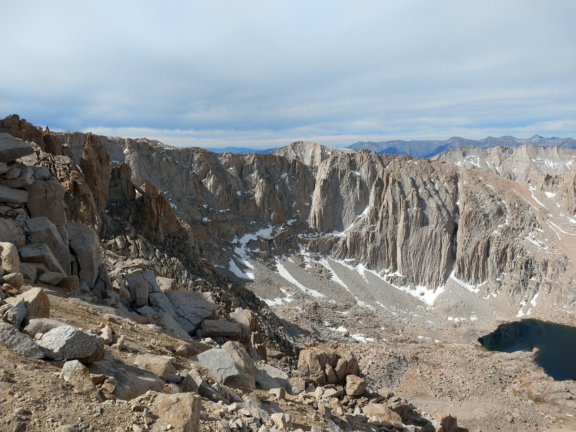 Rugged mountain valley with steep rock walls, snow patches, and a small lake. - Mount Whitney via Cottonwood Lakes and JMT