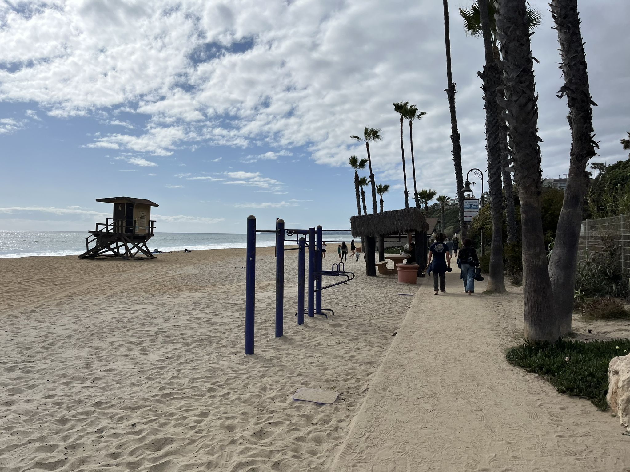 Sandy beach with lifeguard tower, exercise equipment, palm trees, and people walking. - San Clemente Beach Trail