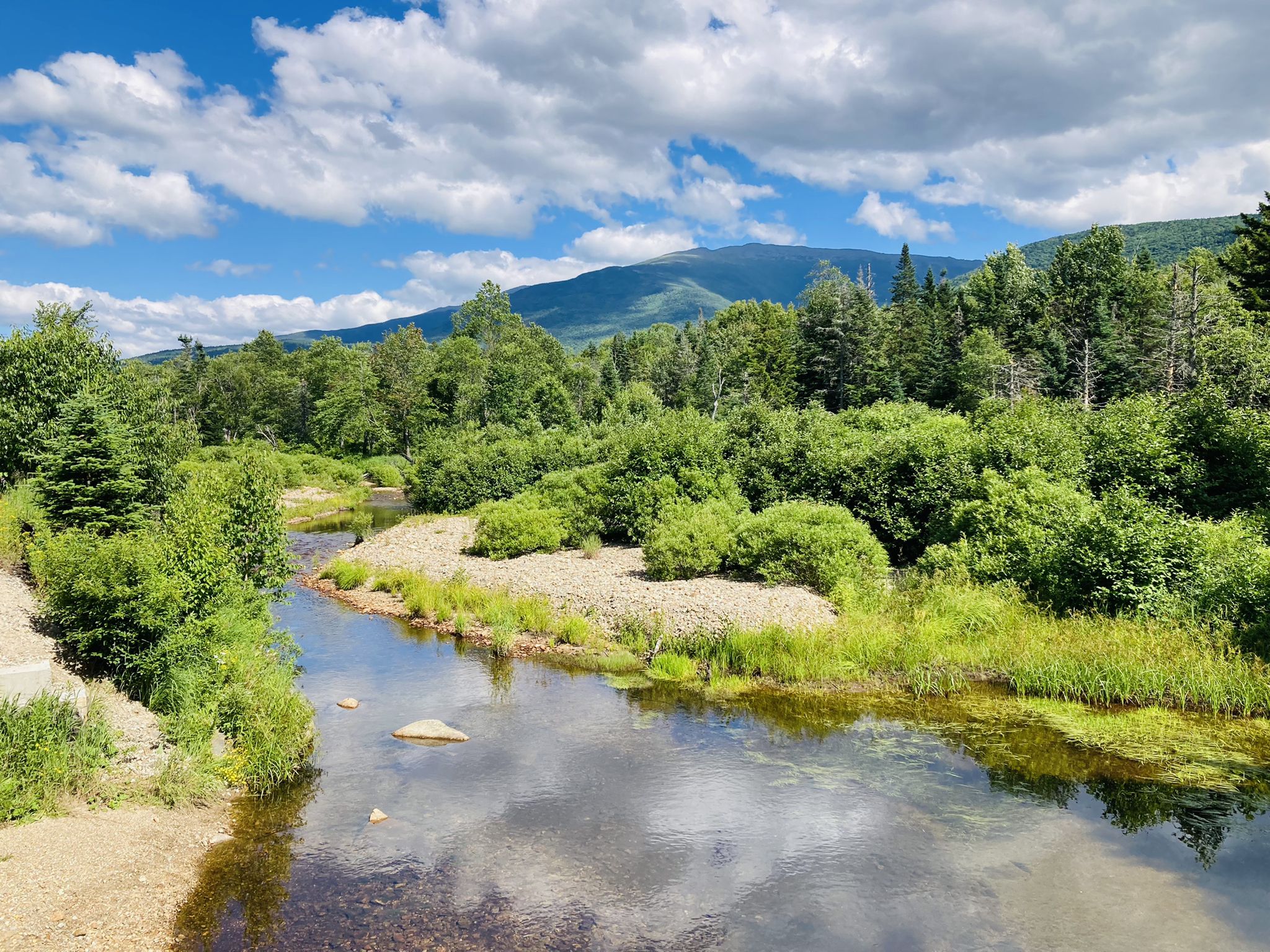 Clear river flowing through a green valley with distant mountains under a bright sky. - Valley Road – Moose Brook State Park loop from Boy Mountain