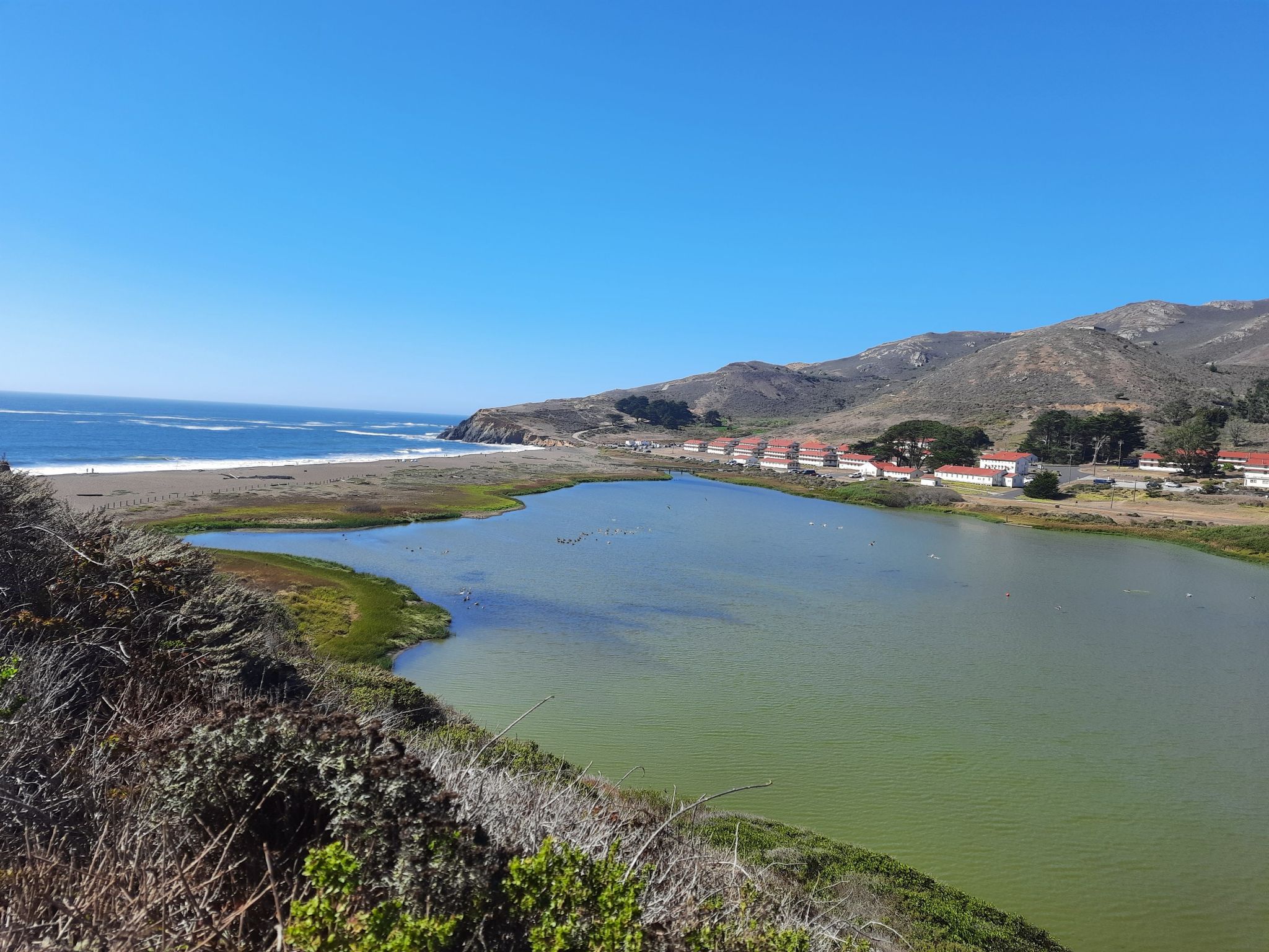 Coastal lagoon next to a sandy beach with ocean waves and distant buildings. - Bobcat and Rodeo Valley Trail Loop