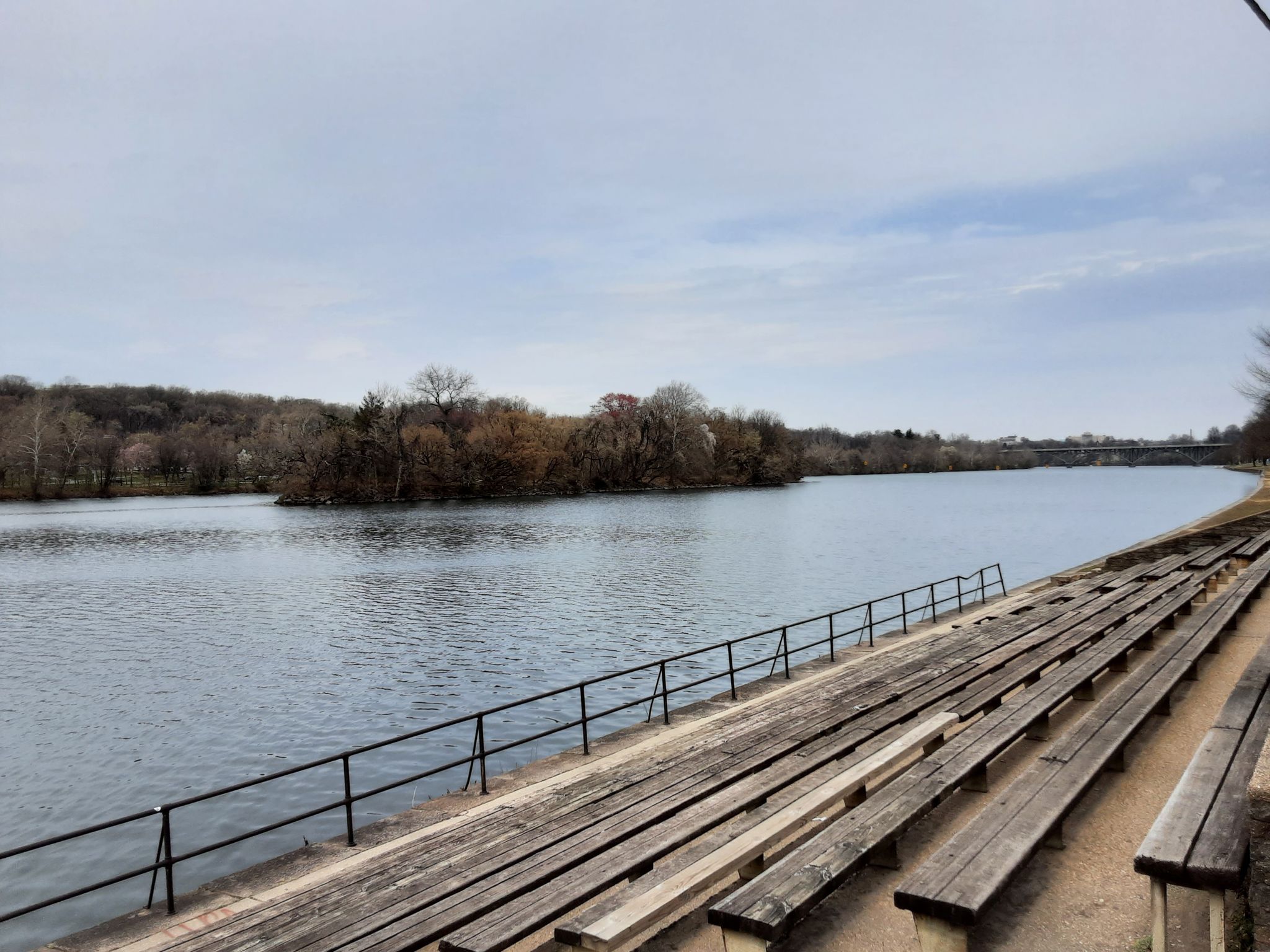 Wide river with empty wooden bleachers, distant island, overcast sky. - John B. Kelly Statue – Playing Angels loop from East Fairmount Park