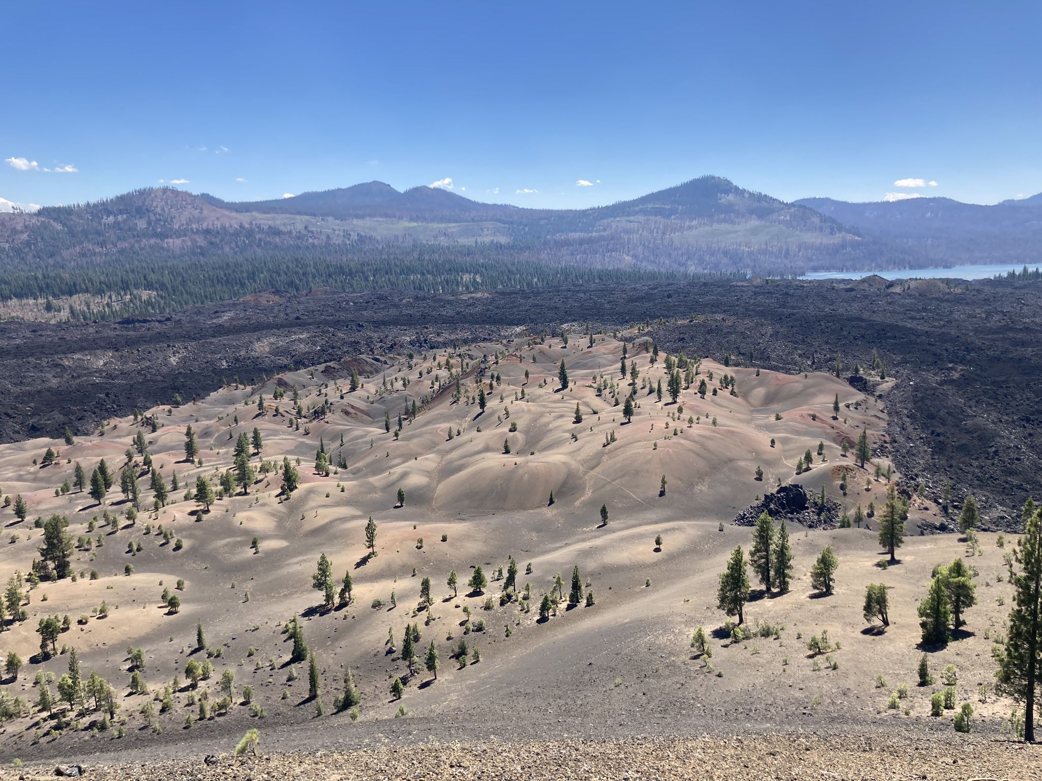 Expansive view of sandy volcanic terrain with scattered trees and distant mountains. - Summit, Horshoe, Snag, Cinder Cone, Rainbow, Twin, and Echo Lakes Loop