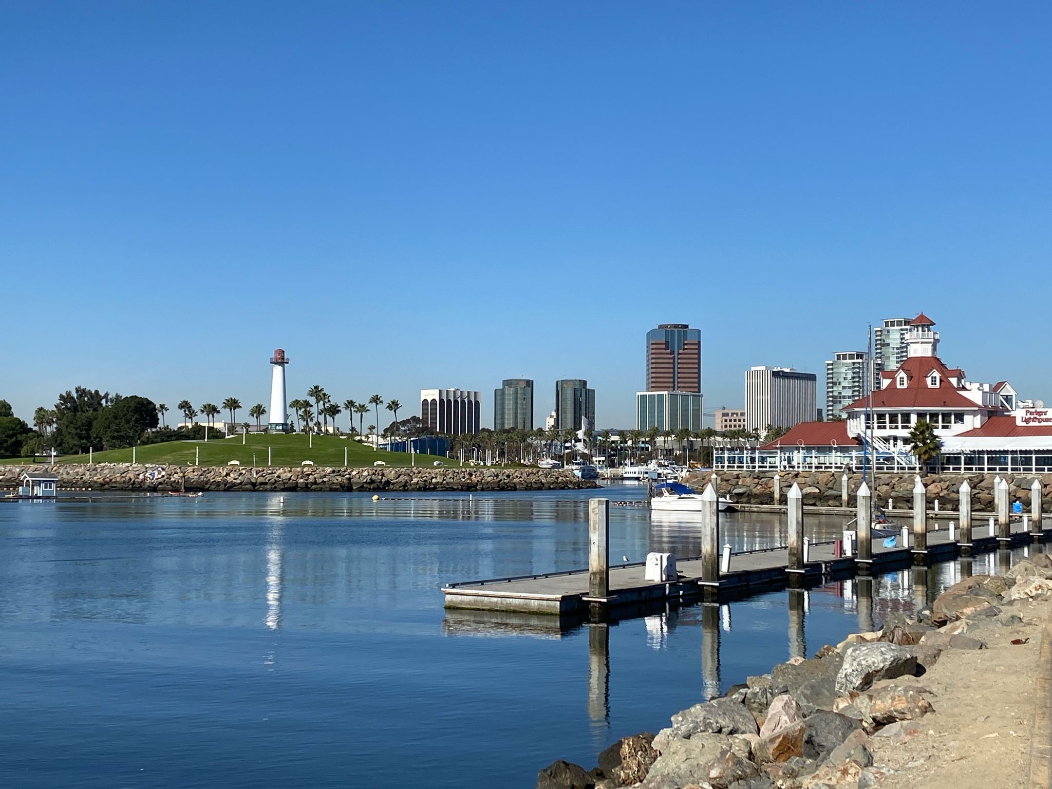 Sunny cityscape with a lighthouse, marina, and distant buildings under clear skies. - Shoreline Beach Bike Path