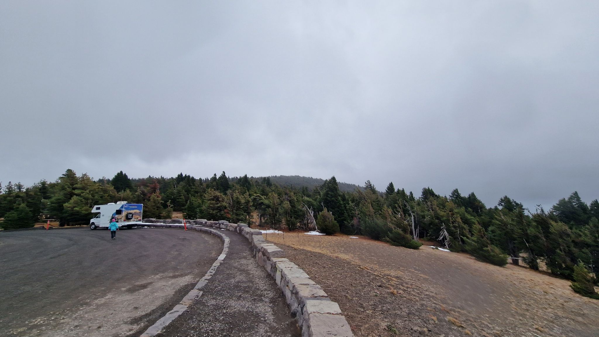 RV and person in a parking area next to a forest under an overcast sky. - East Rim Drive to Cloudcap Overlook