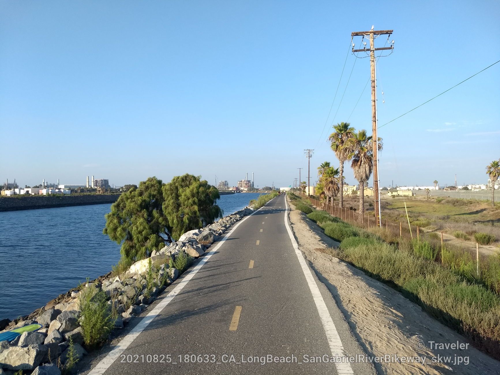 Paved path alongside a river with palm trees under clear sky. - San Gabriel River Trail