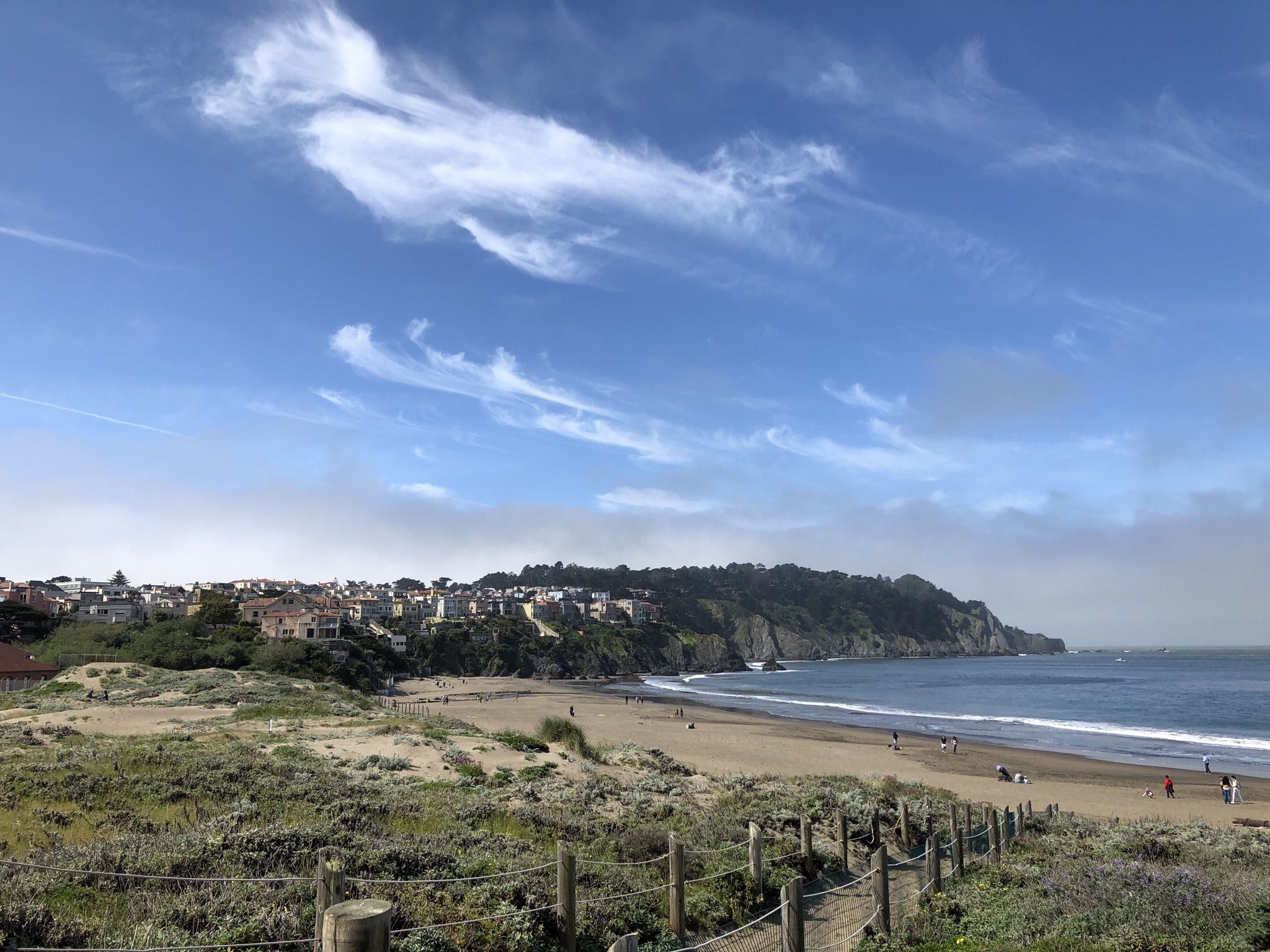 Sandy beach with people, ocean, and a distant town on a sunny day. - Coastal and Lobos Creek Valley Loop