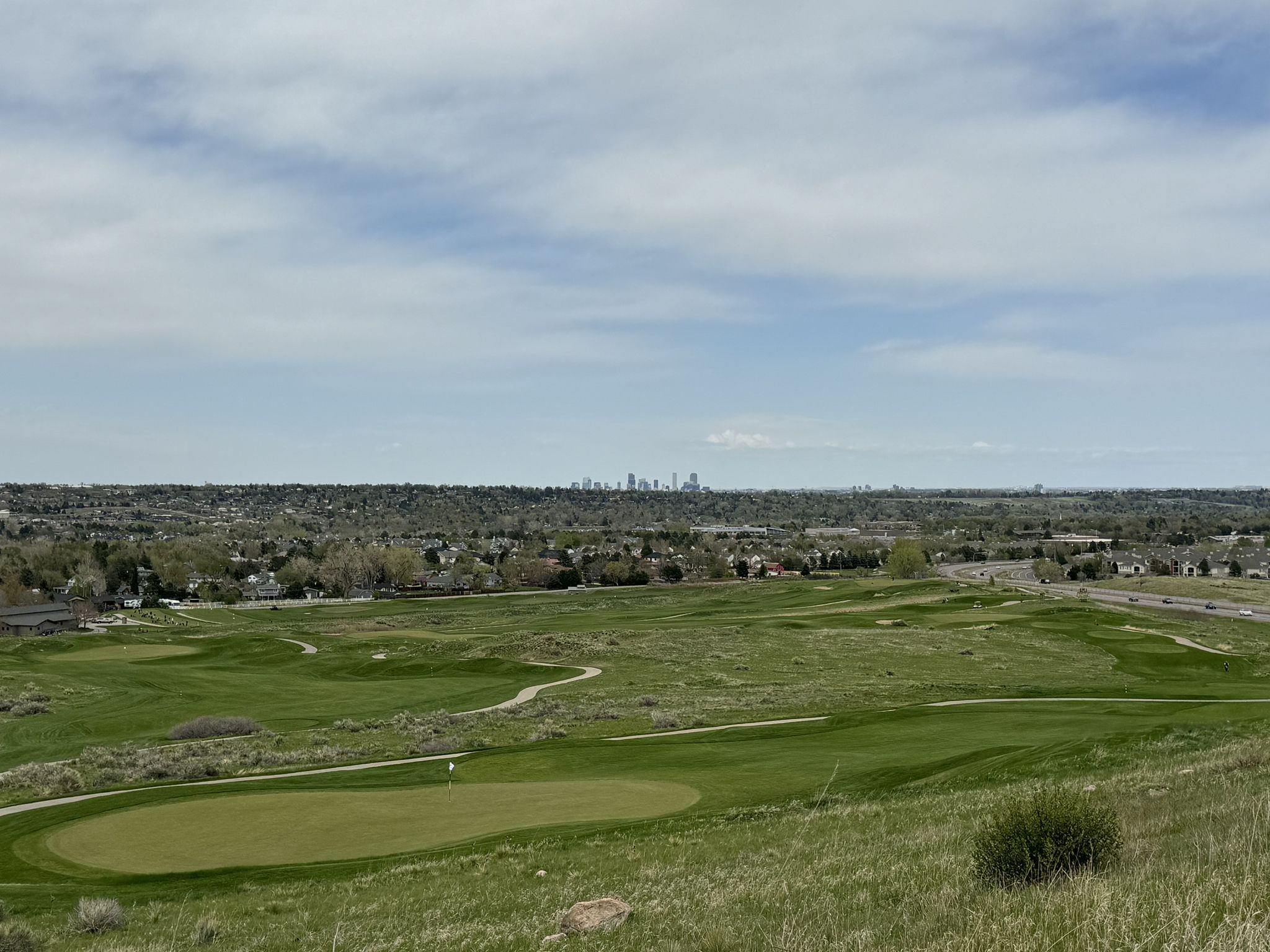 Elevated view of a green golf course with a distant city skyline. - Clear Creek, South Platte River & Bear Creek Trail Loop