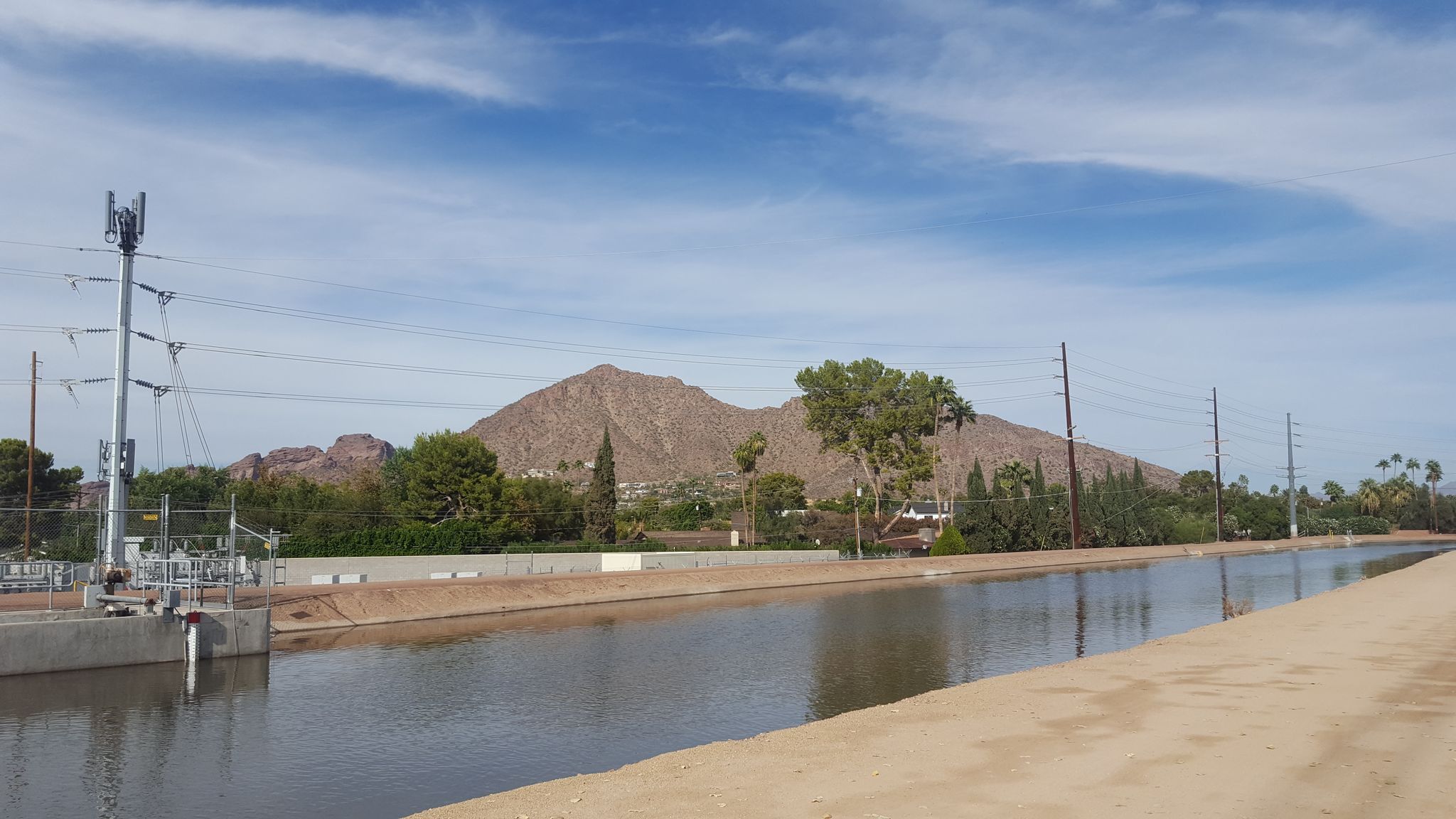 A wide canal with distant mountains and power lines under a partly cloudy sky. - Arizona and Grand Canal Loop