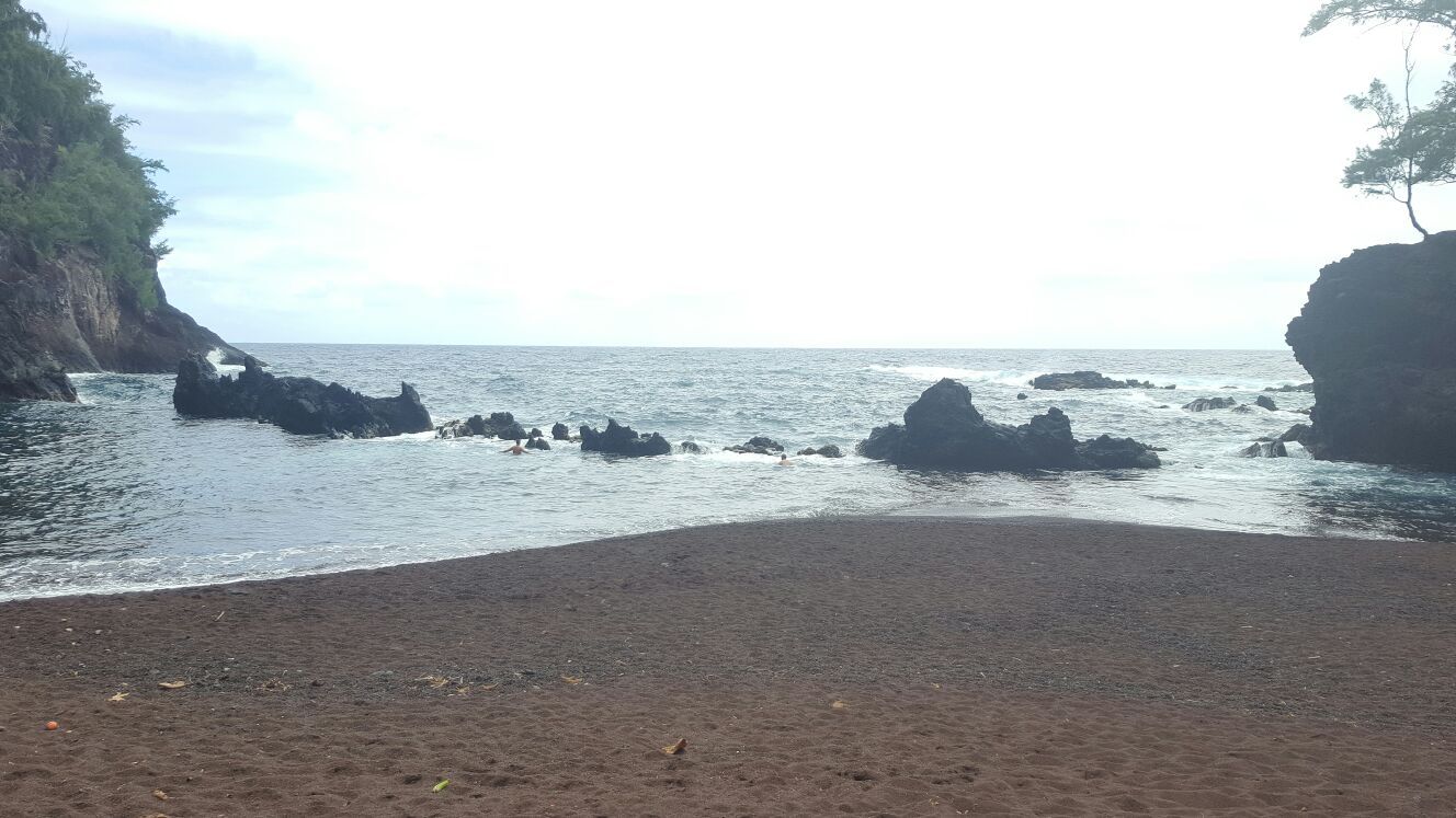 Black sand beach with dark rocks in calm ocean water under an overcast sky. - Koki Beach to Kaihalulu Beach loop