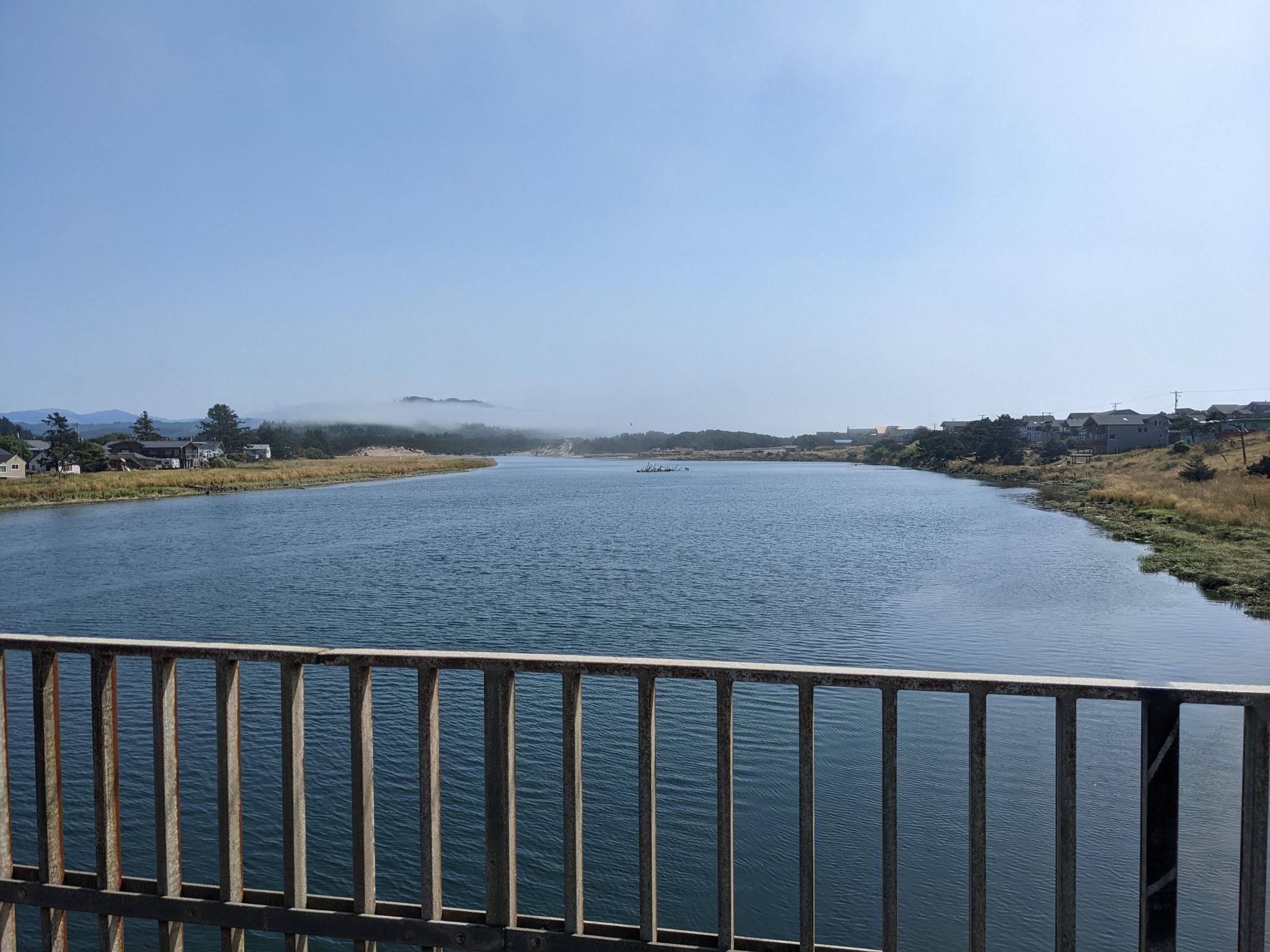 Wide river with distant shore, houses, and low fog under clear sky. - Pacific City loop