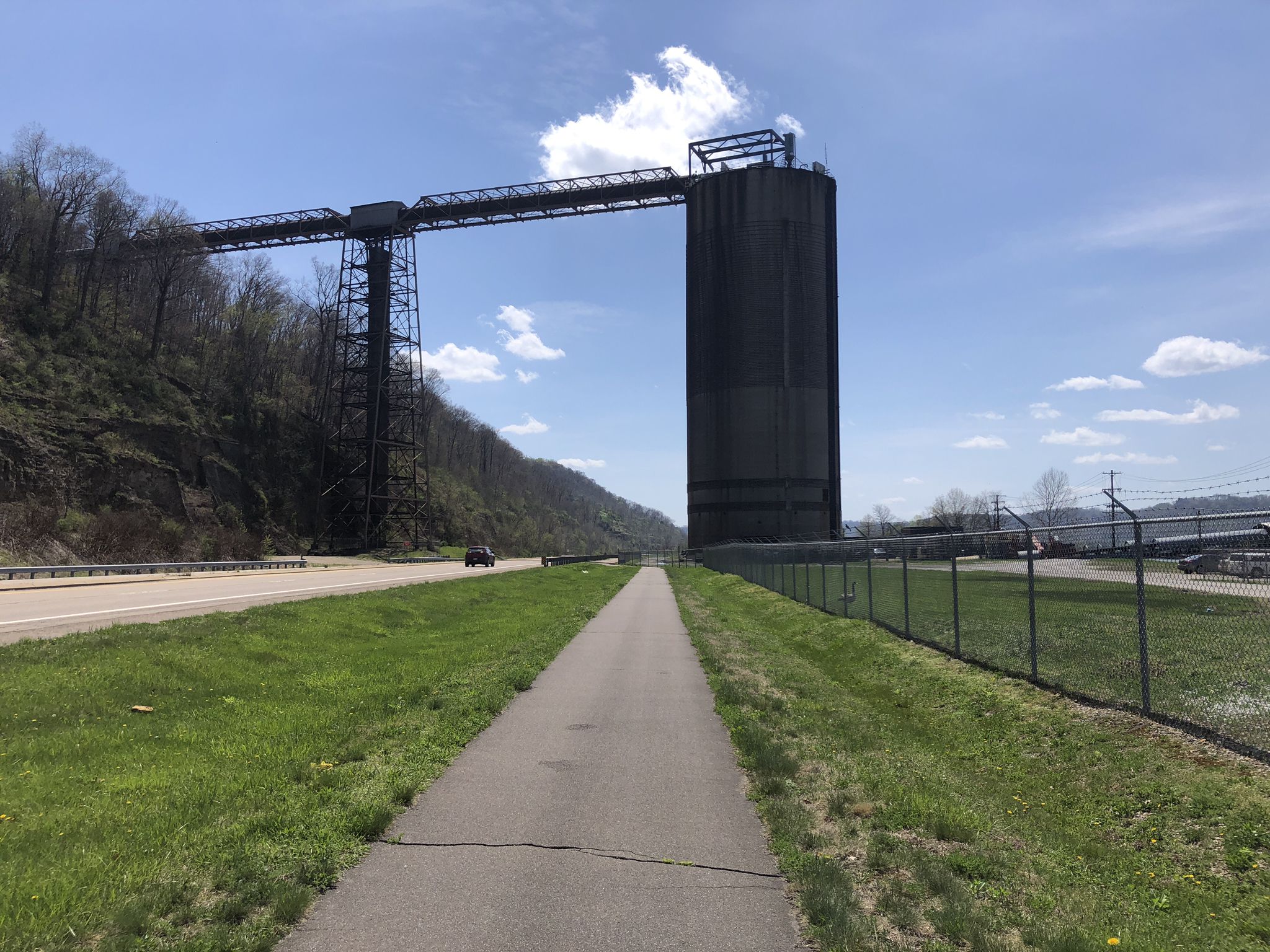 A large industrial structure looms over a path and highway on a sunny day. - Hempfield Tunnel loop from Greggsville