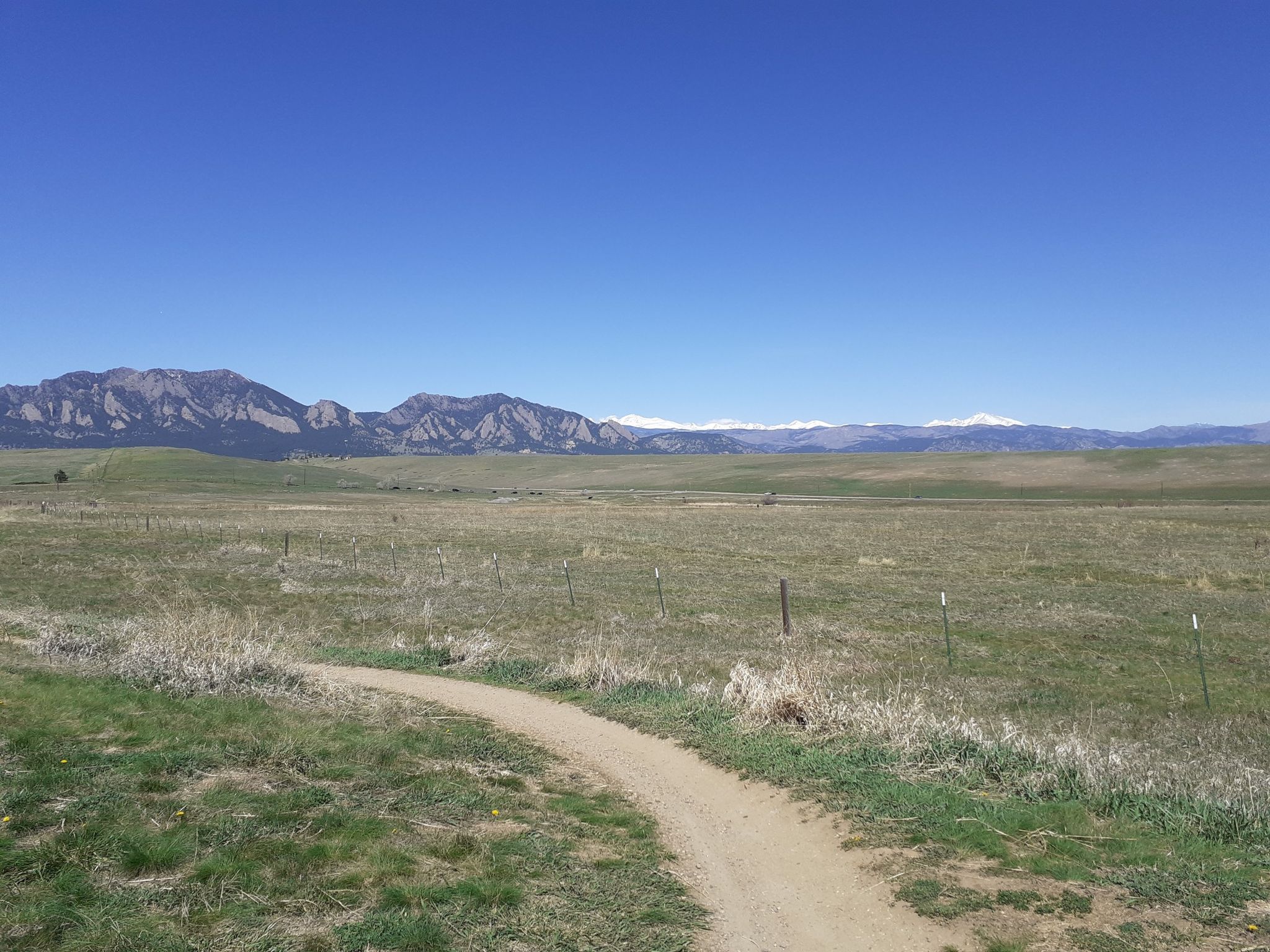 Dirt path through green field towards distant snow-capped mountains. - Mayhoffer Trail loop from Flatiron Crossing