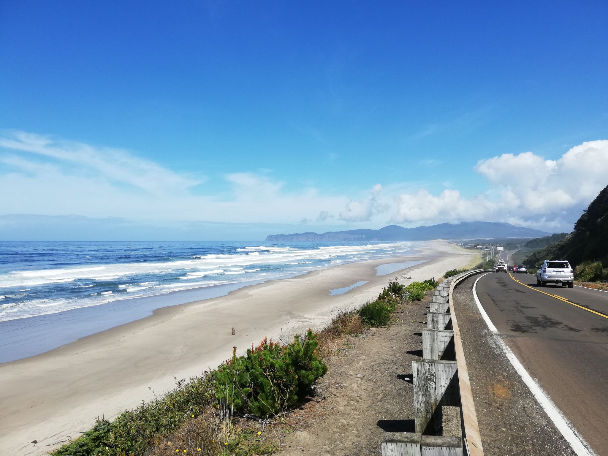 A coastal highway runs beside a wide sandy beach and blue ocean. - Pacific City – Pelican Pub & Brewery loop from Pacific City