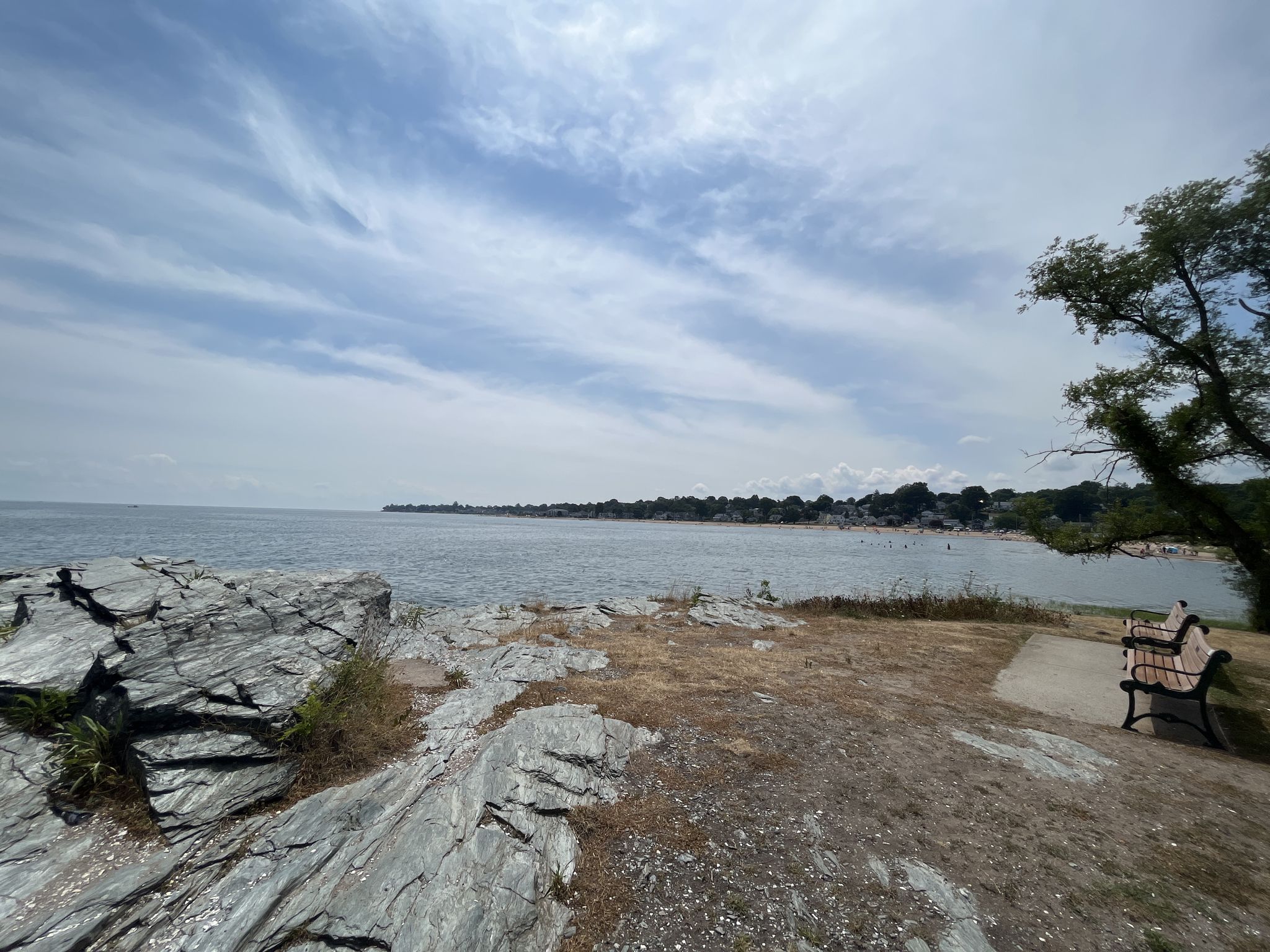 Rocky coastline overlooking a calm ocean and distant sandy beach under cloudy skies. - Bradley Point Park loop via Beach Street Trail