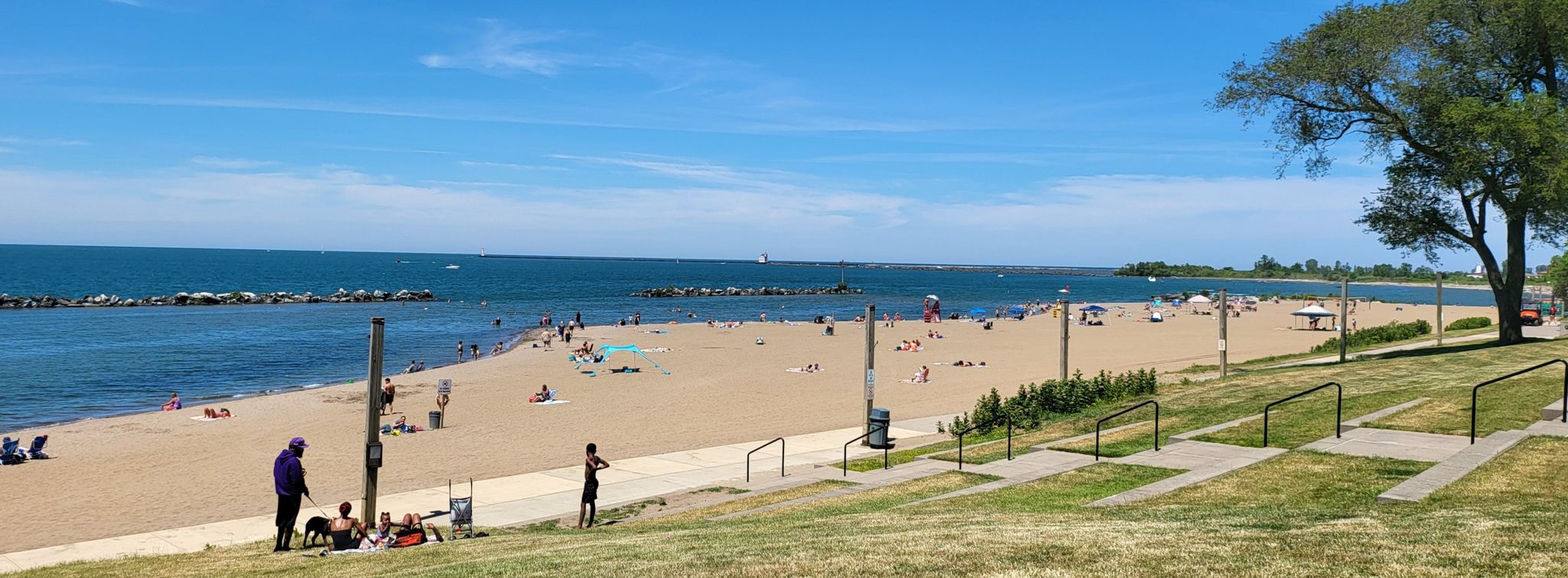 Sunny beach with many people, blue ocean, and green grassy slope. - Lakeview Park loop