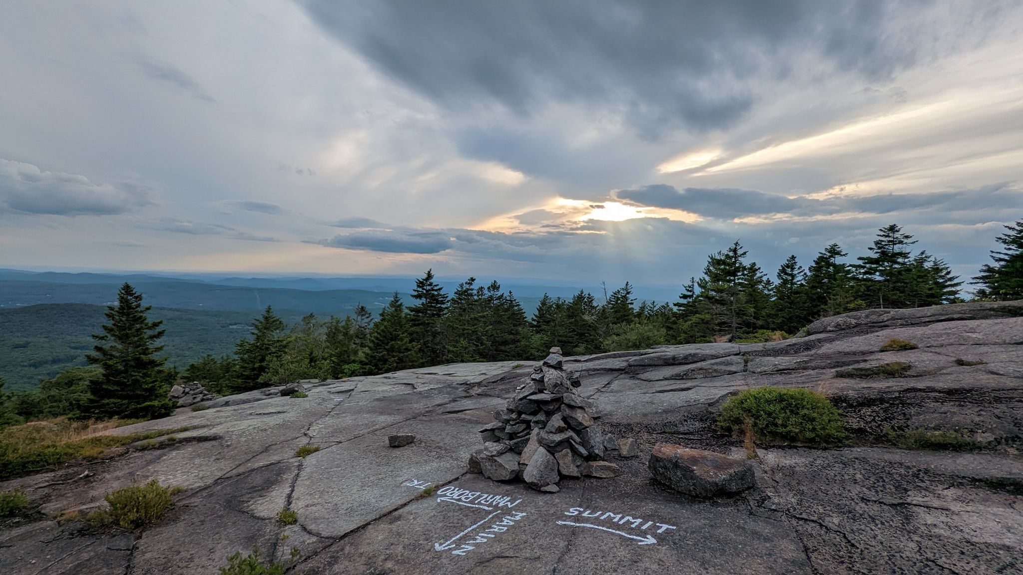 Rocky summit with a stone cairn and path arrows under a cloudy sky. - Marlboro Trail