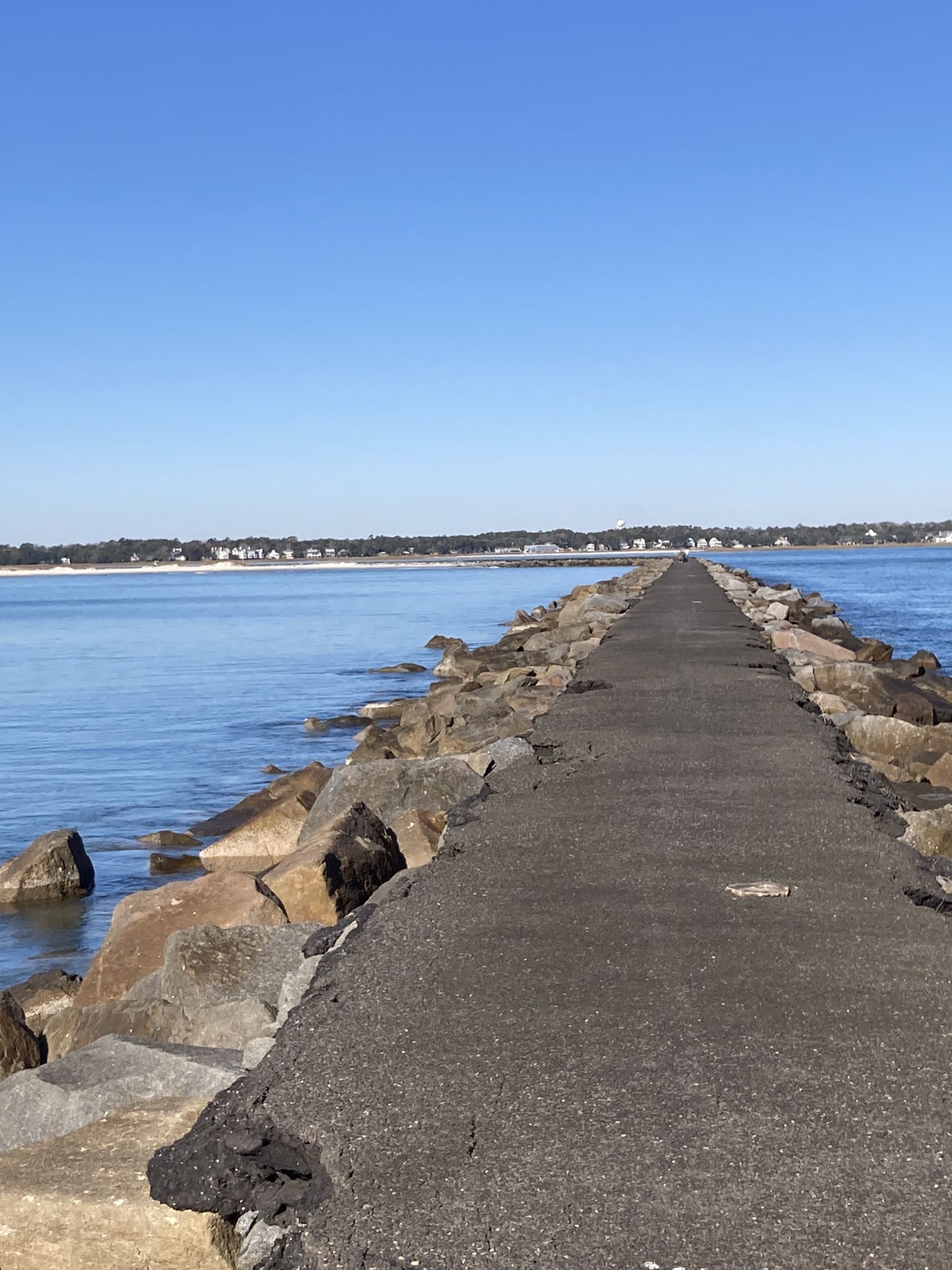 A long rock jetty extends into calm blue water under a clear sky. - Huntington Beach Jetty Trail