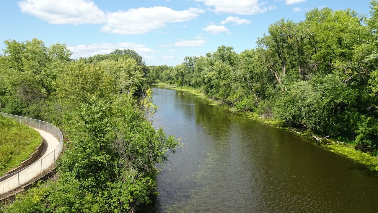 A calm river flows through dense green trees under a bright blue sky. - Mississippi River & Apple Blossom Scenic Byway loop