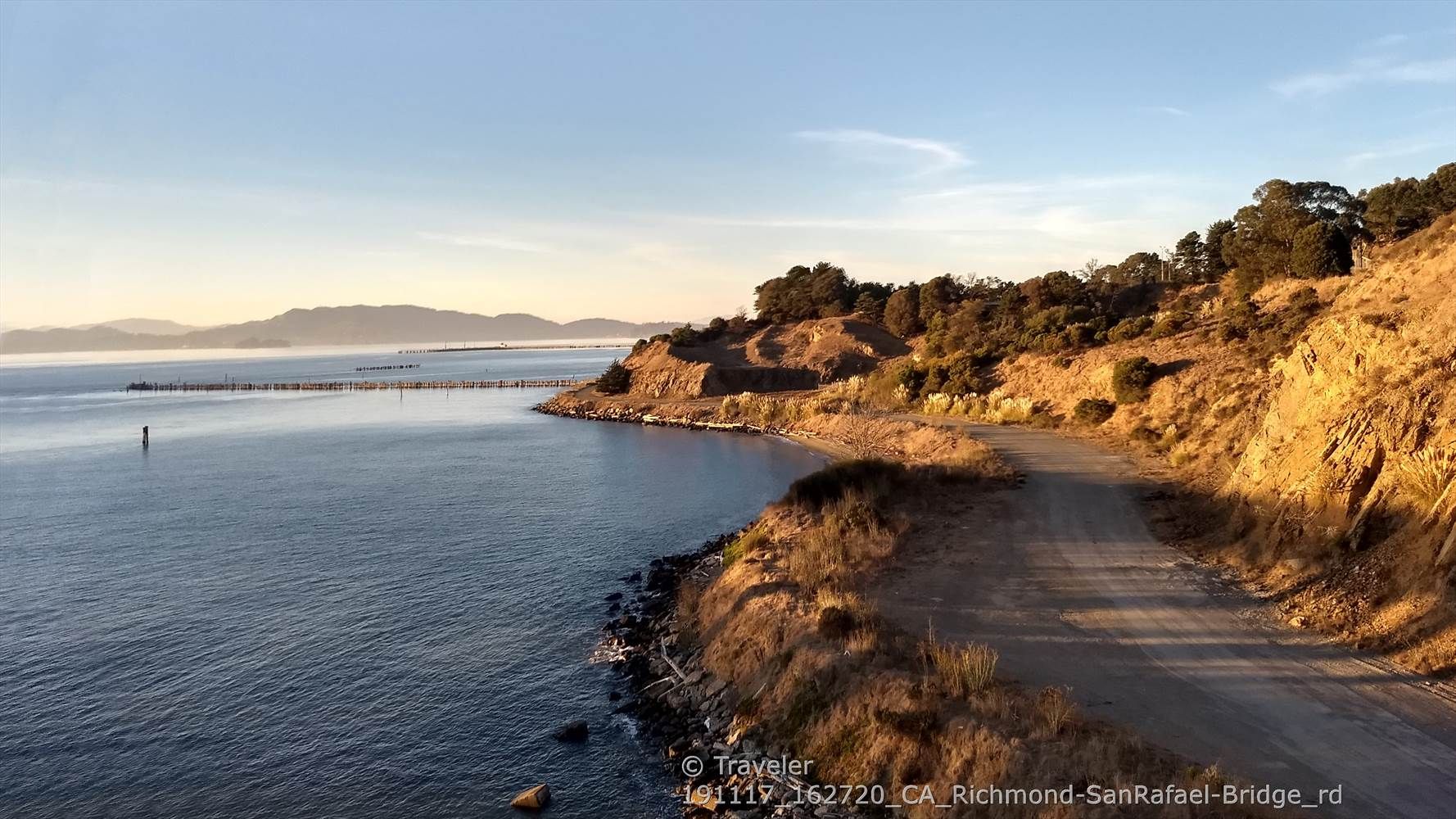 Dirt road curves along a rocky coast beside calm water at sunset. - Horse Hill Bike Path – Sausalito Path loop from Richmond