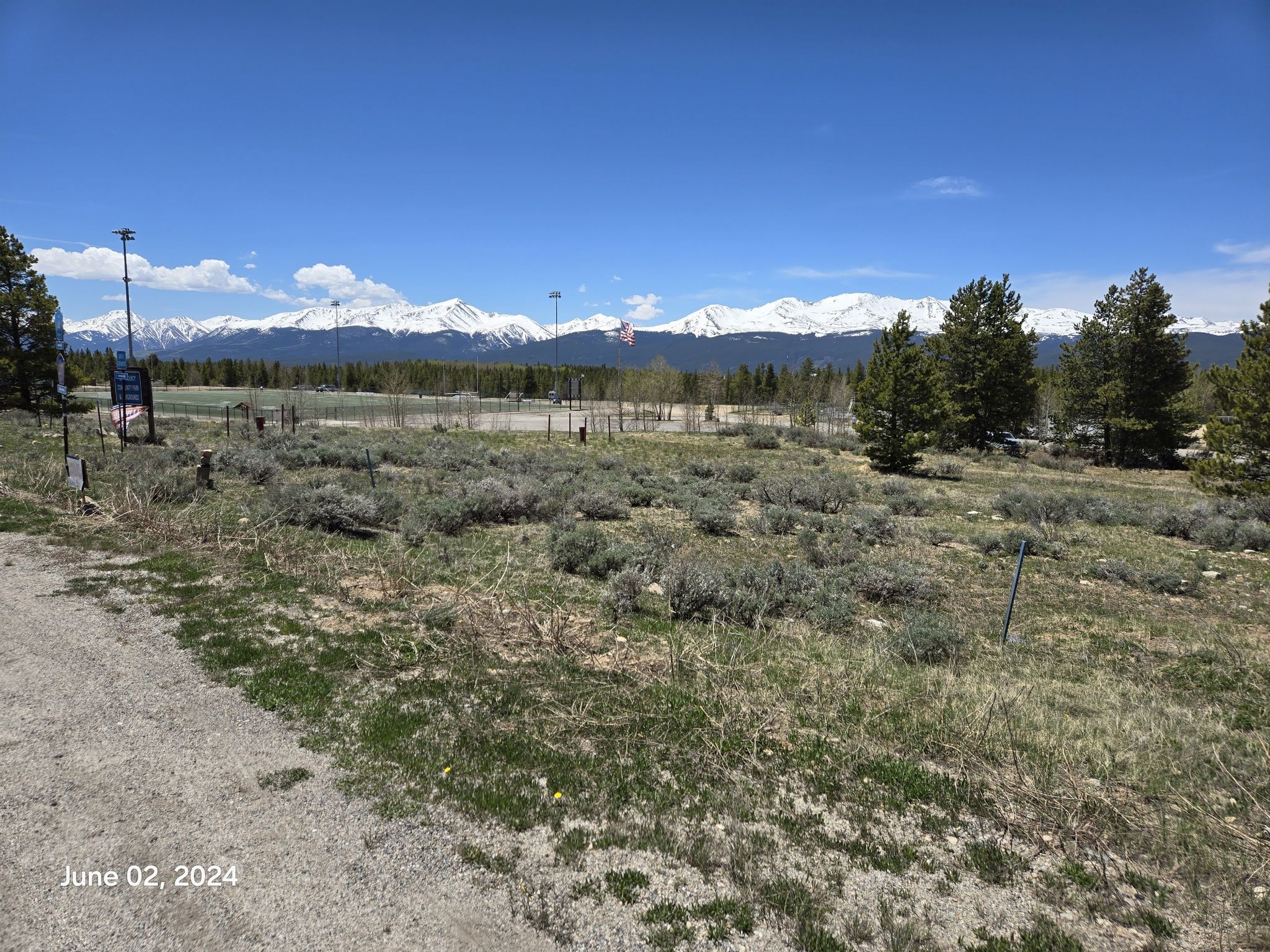 A vast grassy field with distant snow-capped mountains under a blue sky. - Turquoise Lake loop