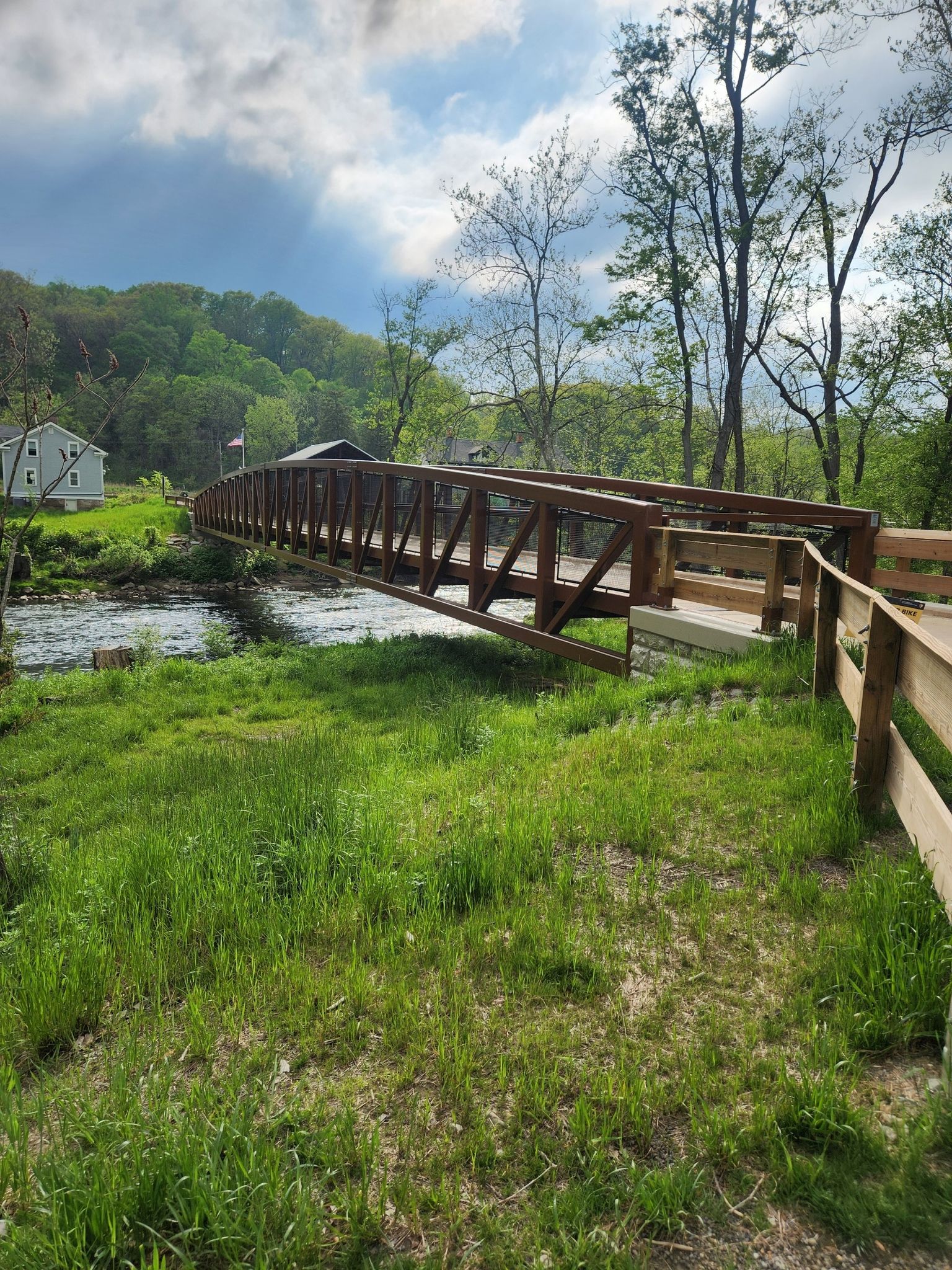 A long wooden bridge spans a river, surrounded by green grass and trees. - Jaite Mill Bridle and Buckeye Trail Loop