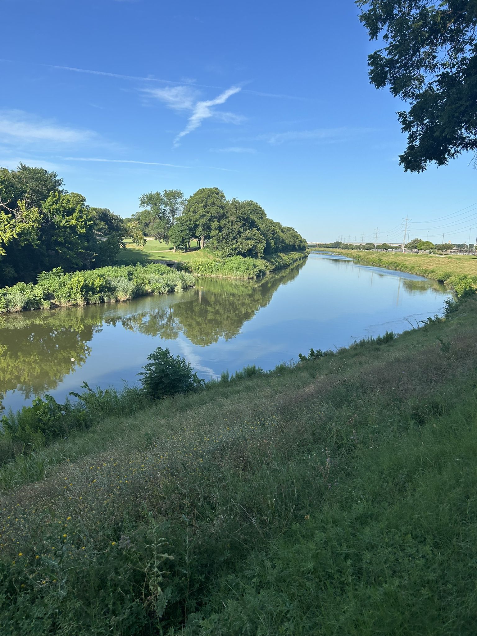 Calm river reflecting trees and blue sky, with grassy banks. - Benbrook Lake – Trail along the Trinity river loop from Sycamore School & Hulen