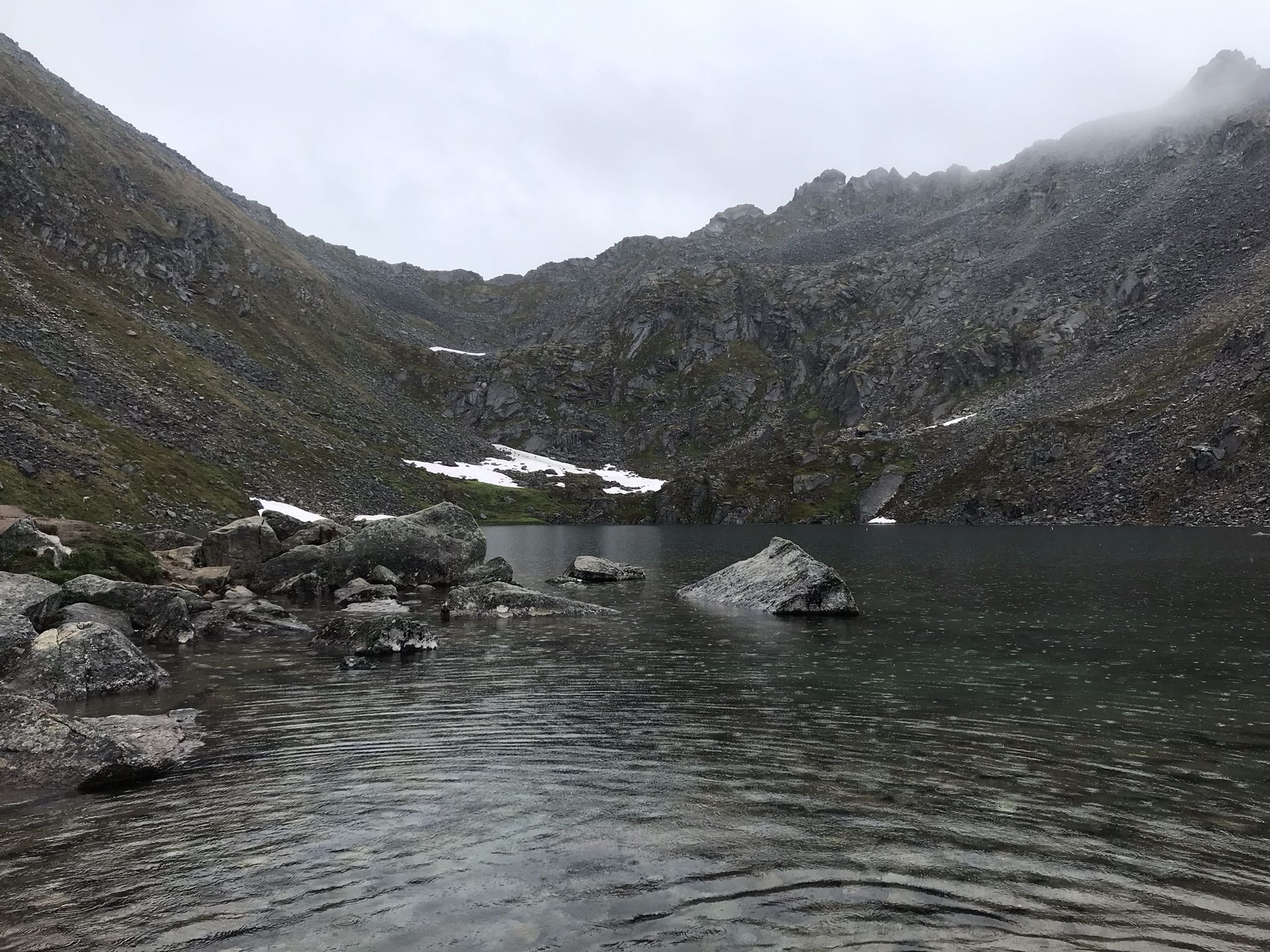 Dark mountain lake surrounded by rocky slopes under an overcast sky. - Gold Cord Lake Trail