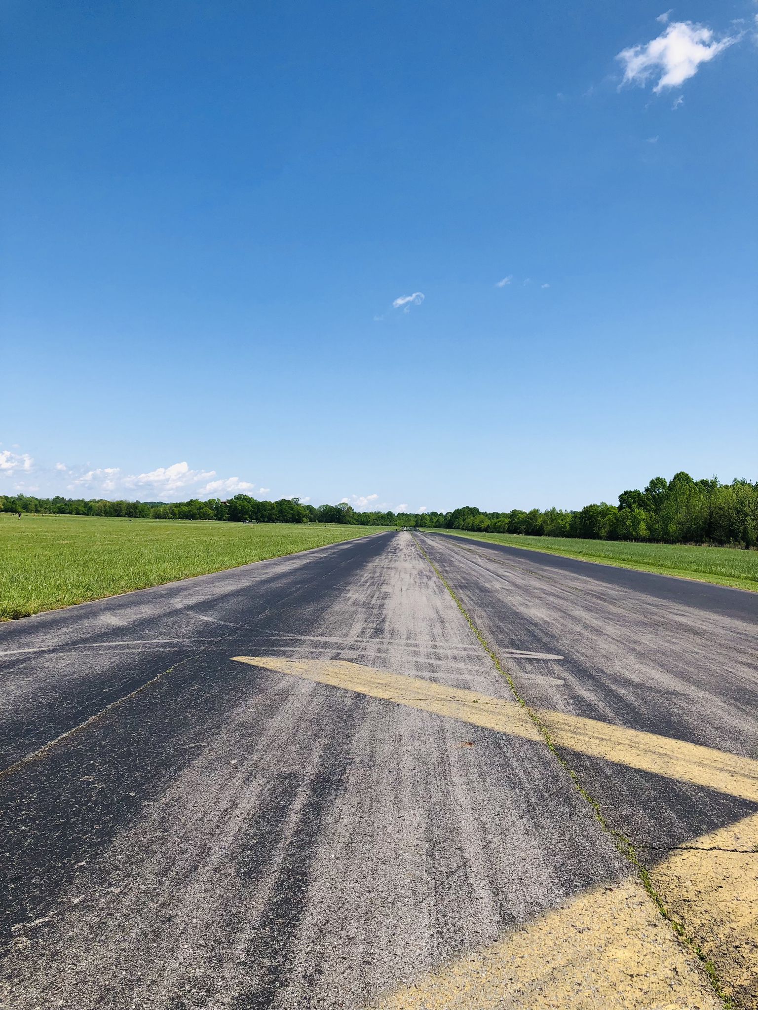 Long asphalt path with yellow markings, bordered by green fields under blue sky. - Cornelia Fort Airpark Runway Loop