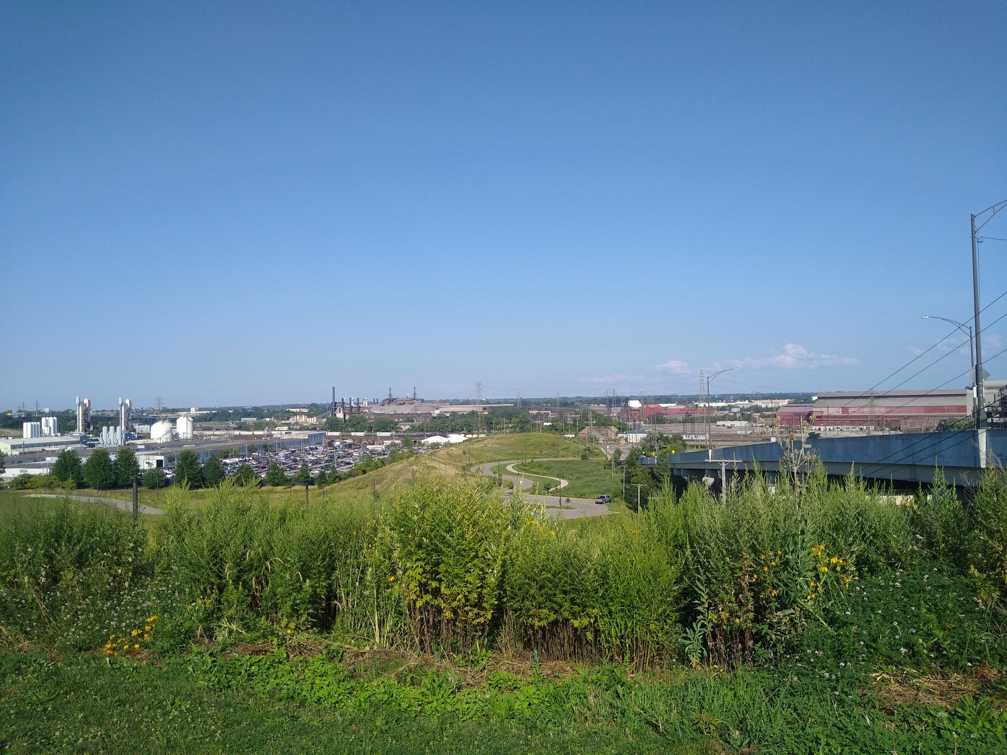 Industrial landscape viewed from a grassy hill under a clear blue sky. - Ohio & Erie Canal Towpath Trail